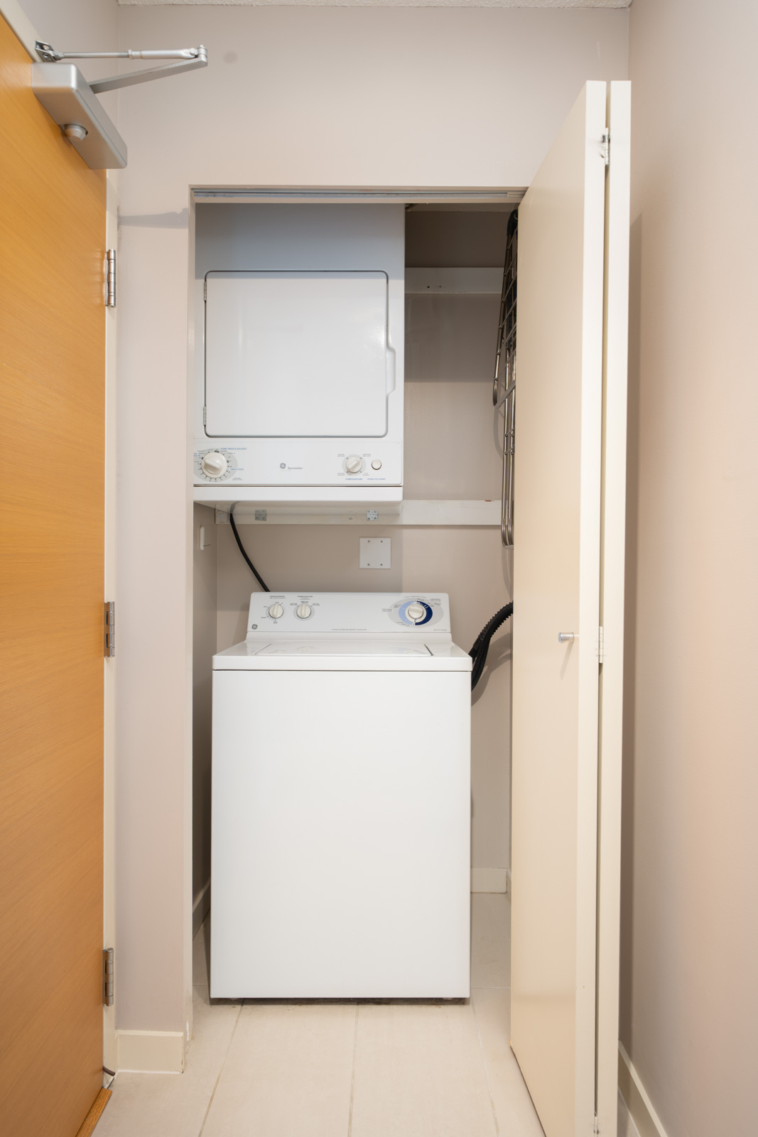 Stacked washer and dryer in a compact laundry closet with beige walls and an open white door at 909 Mainland St, Vancouver.