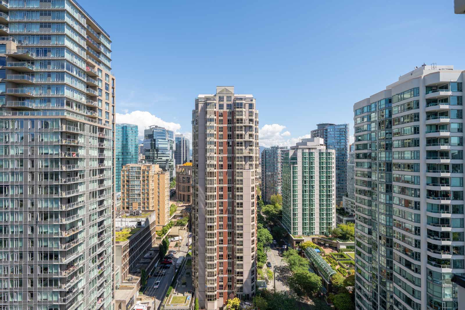 High-rise apartments, green trees, and streets seen from the 23rd floor at 909 Mainland St under a clear blue Vancouver sky.