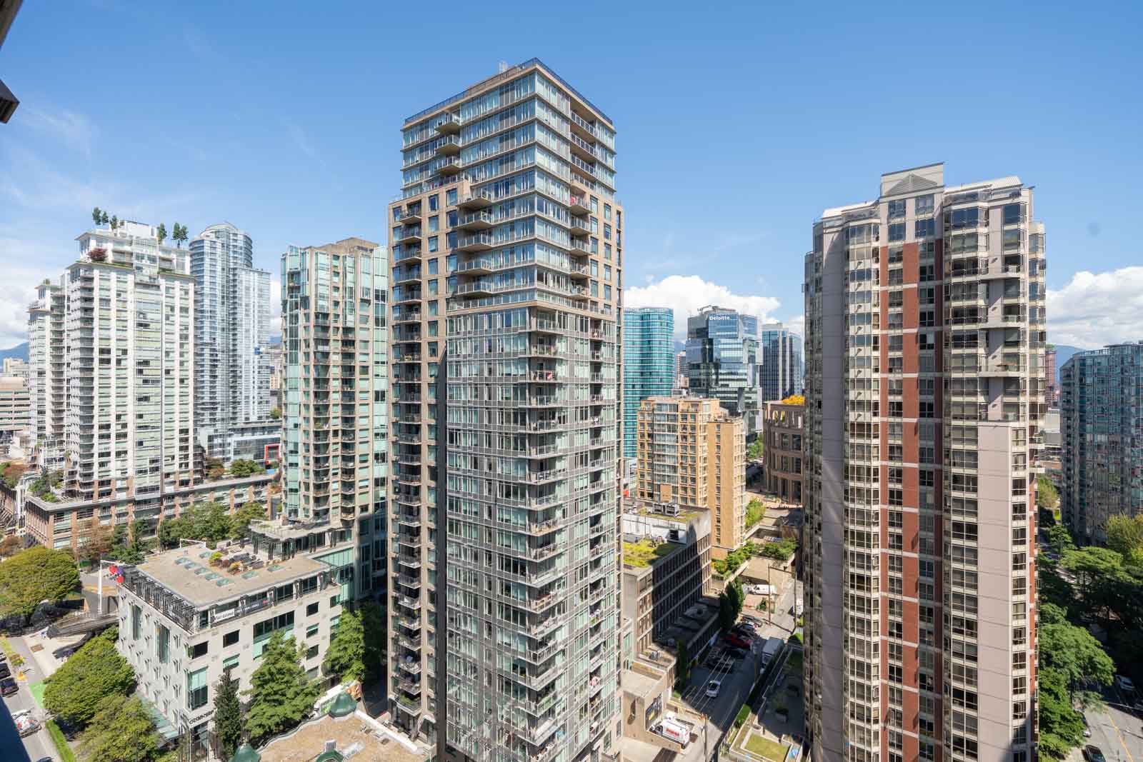 Vancouver high-rises and offices tower above tree-lined streets, including Mainland St, seen from the 23rd floor under clear skies.