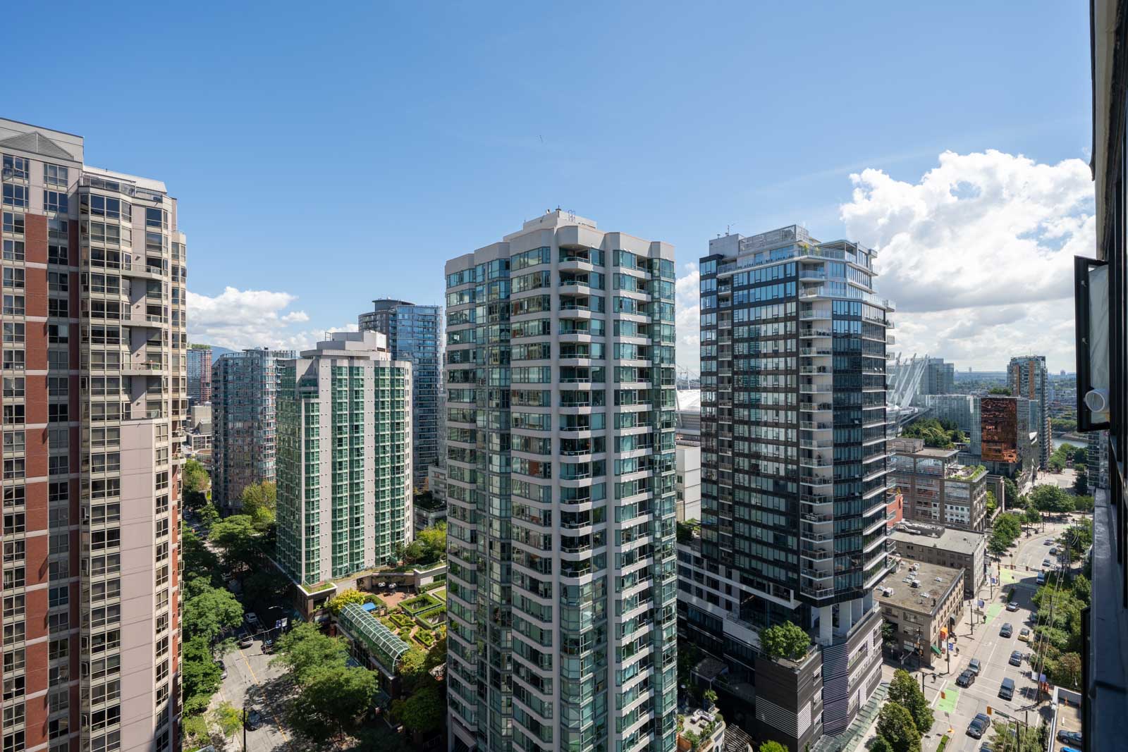 High-rise residential towers with glass balconies overlook street and greenery near 909 Mainland St, Vancouver, under blue sky.