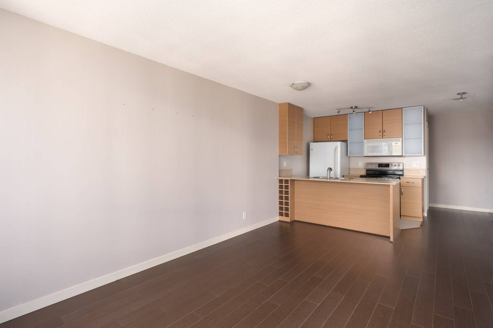 Unfurnished modern kitchen and living area on 23rd floor, Mainland St, Vancouver; light wood cabinets, white appliances, brown floors.