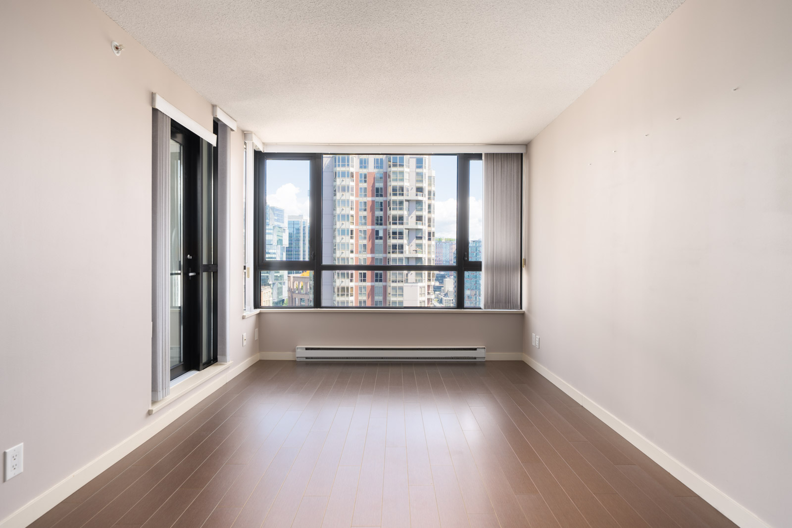 Empty apartment with light wood floors, beige walls, large window overlooking Vancouver from the 23rd floor, and a glass door left.