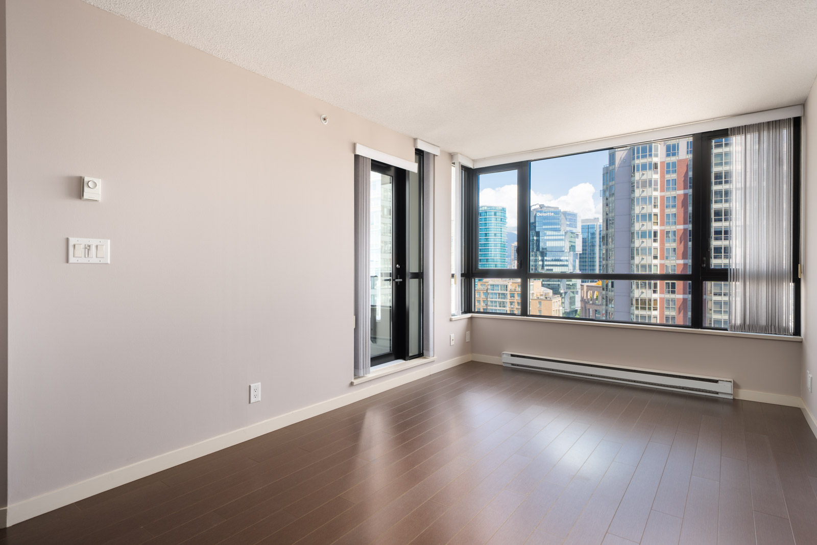 Unfurnished apartment room with large windows, city view, beige walls, hardwood floors, and balcony on Mainland St in Vancouver.