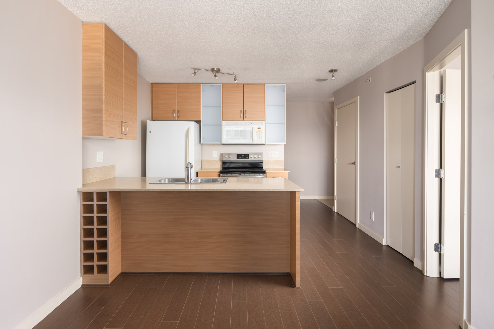 Modern kitchen at 909 Mainland St, Vancouver with light wood cabinets, white appliances, island sink, brown floors, and beige walls.