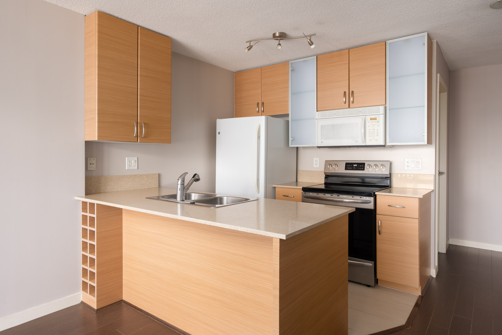 Modern kitchen with light wood cabinets, white appliances, double sink, beige island with wine rack on 23rd floor, Vancouver.
