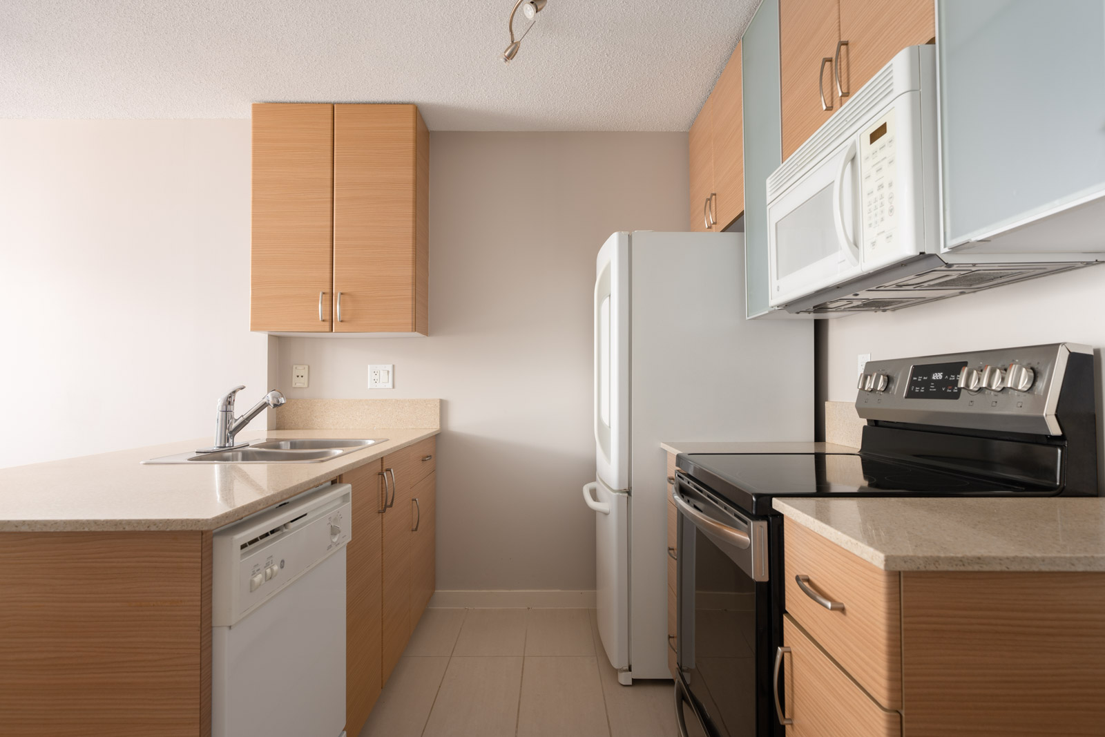 Modern kitchen with light wood cabinets, white appliances, and beige countertops on the 23rd floor in Vancouver.