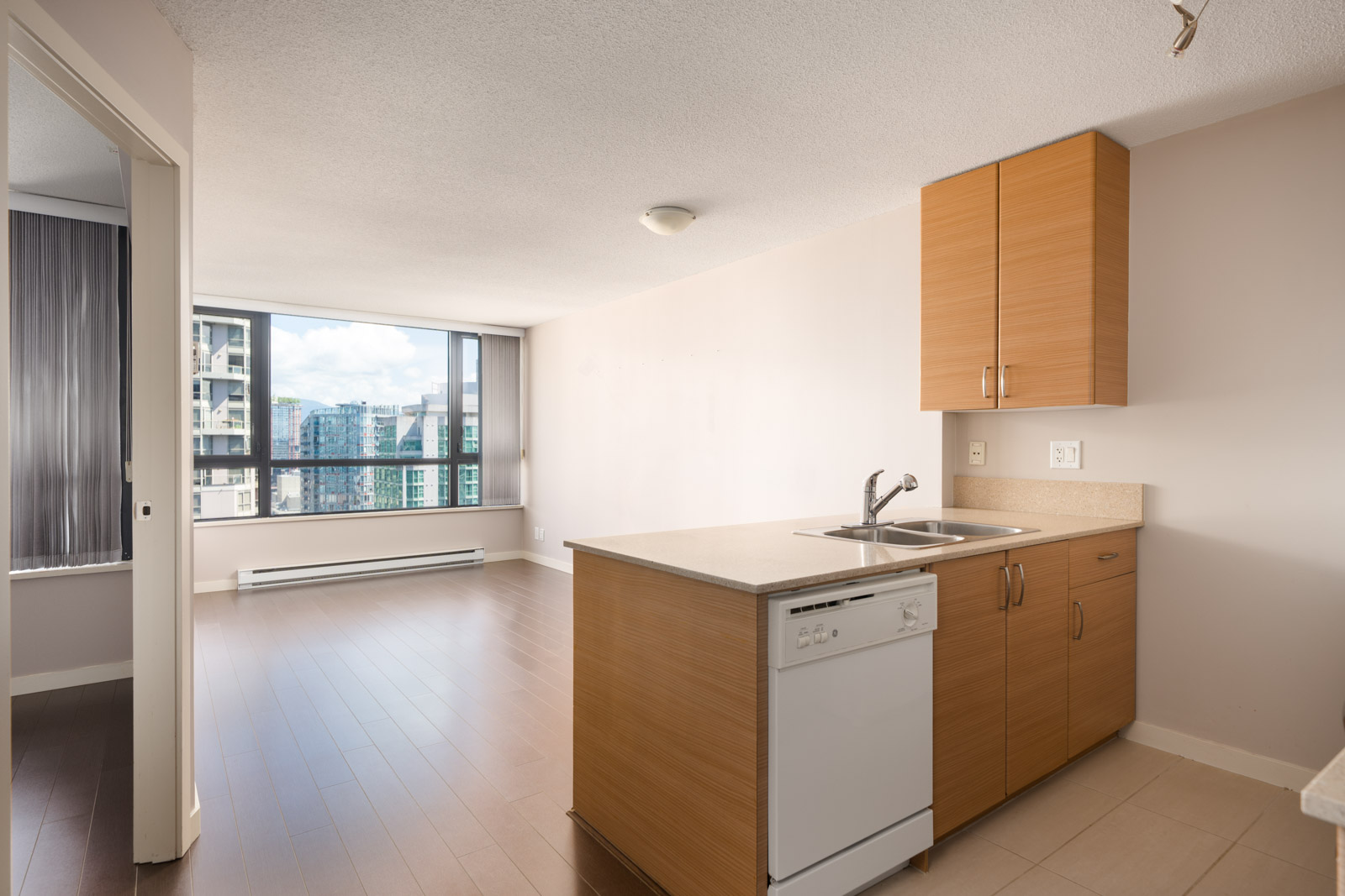 Modern 23rd-floor Vancouver apartment with wood floors, kitchen island, large window with city views, and side room visible.