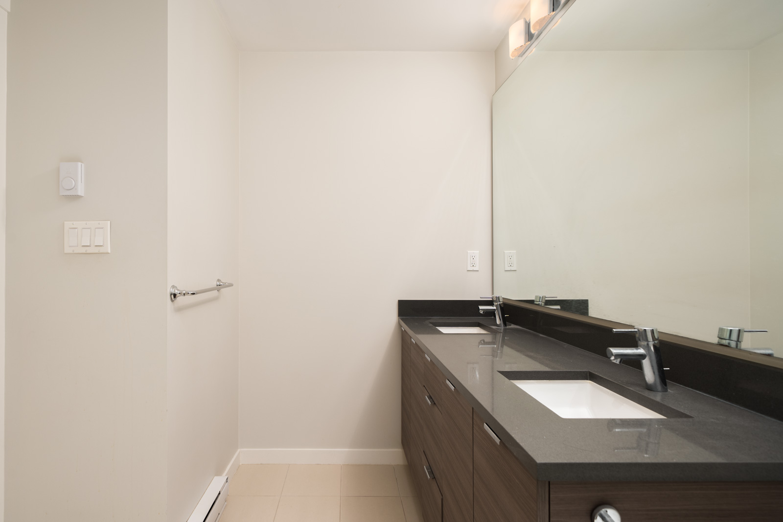 Contemporary bathroom with double sinks, dark counter, large mirror, and pale walls in a North Vancouver residence. No decor visible.
