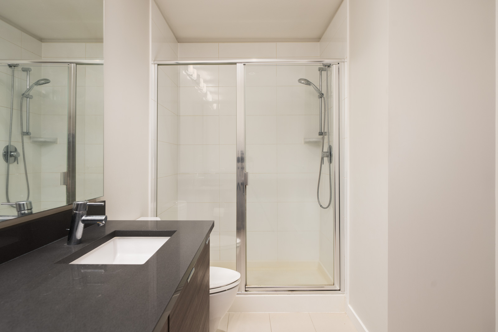 Modern North Vancouver bathroom with glass shower, white tile walls, black vanity, sink, and wall-mounted showerhead.