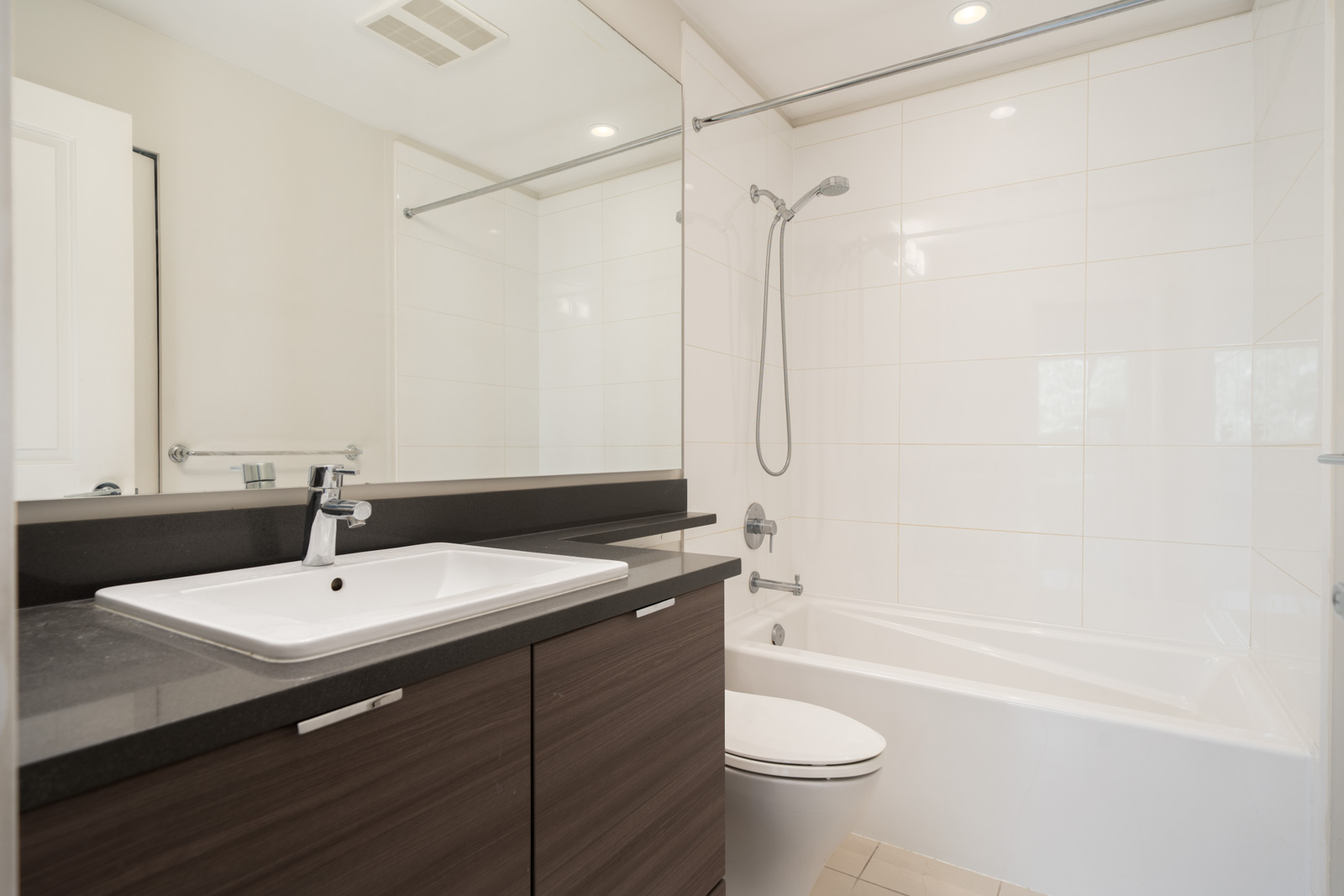 Modern bathroom featuring a dark wood vanity, white sink, wall mirror, and a tub-shower with white tile near North Vancouver’s Mountain Hwy.