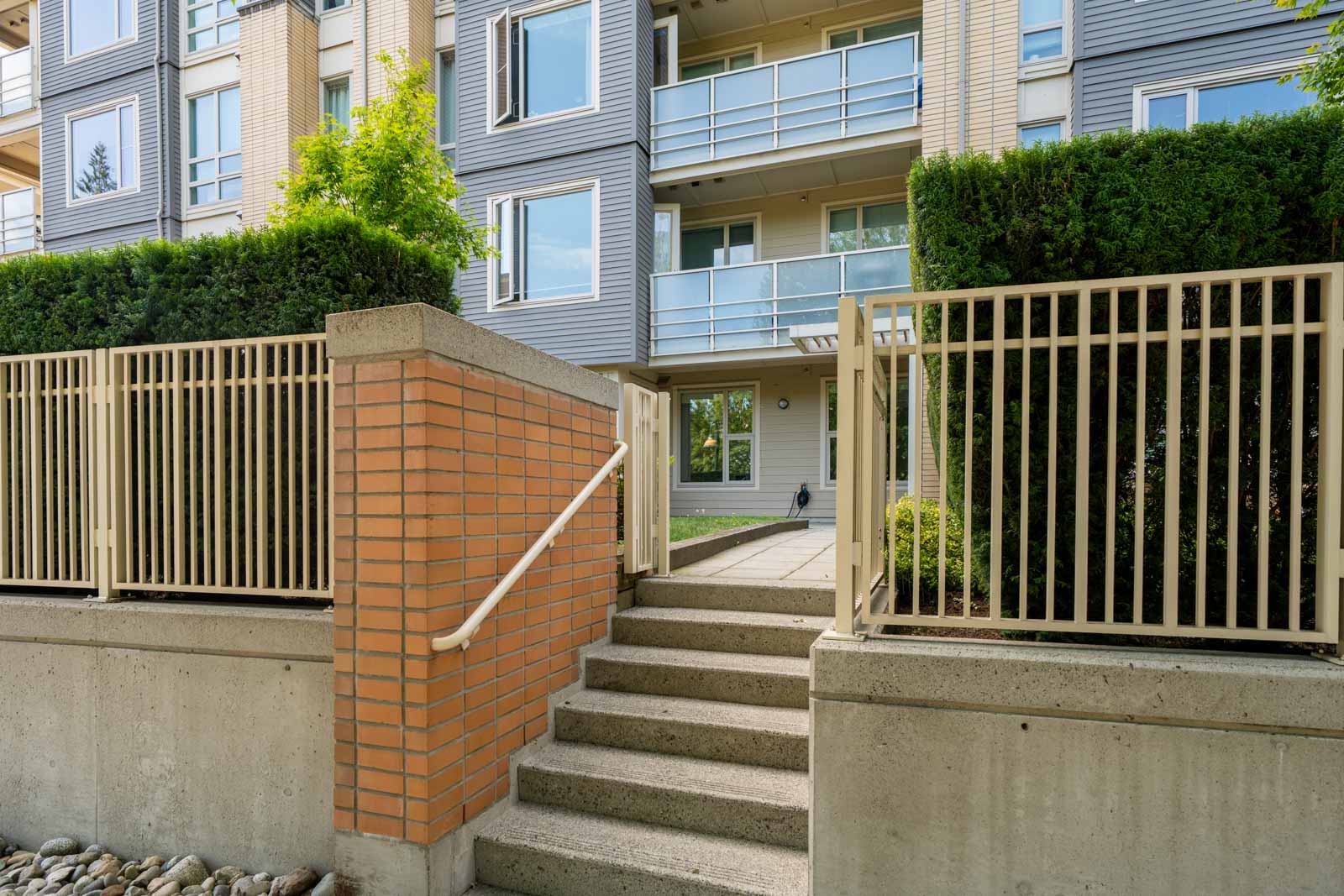 Concrete steps with a handrail lead to a gated entry at a modern apartment with balconies on Mountain Hwy, North Vancouver.