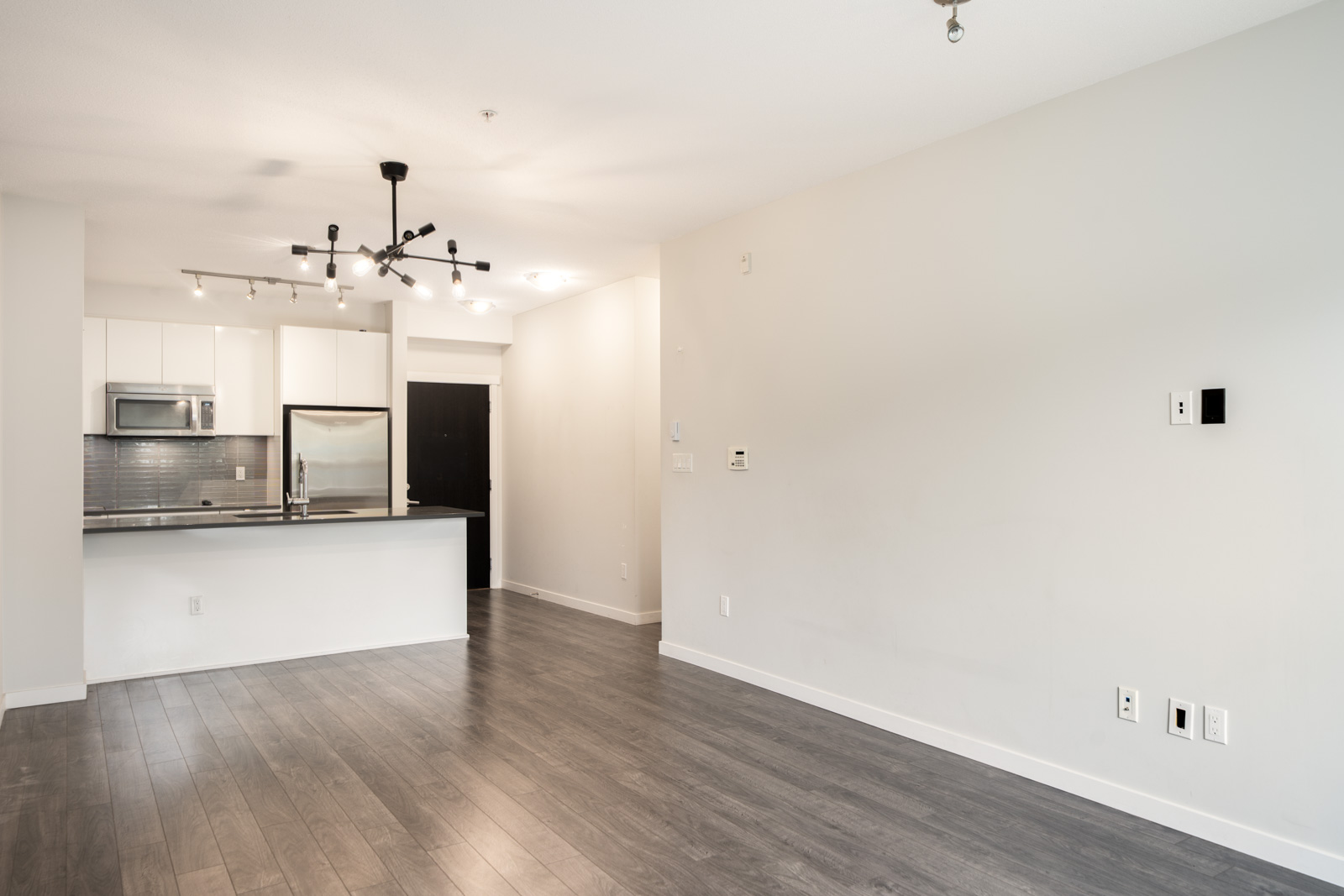 Unfurnished modern apartment on Mountain Hwy, North Vancouver: open kitchen, stainless appliances, light walls, gray wood floors.