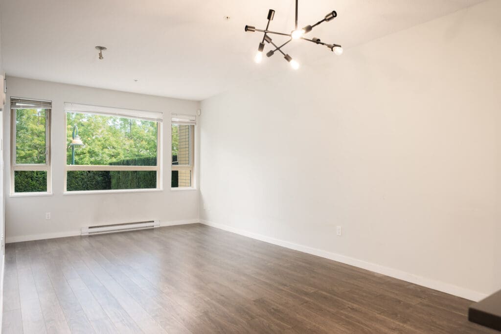 Unfurnished room in North Vancouver near Mountain Hwy, with large windows, white walls, wood floor, and black ceiling light.