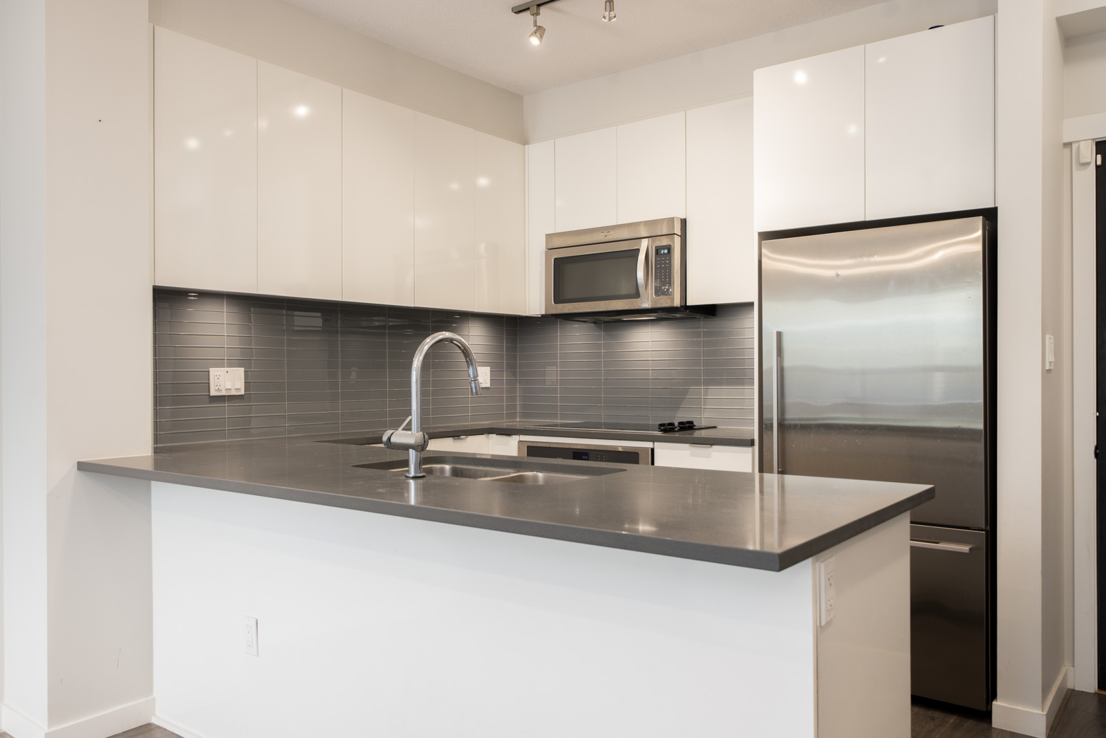 Modern North Vancouver kitchen with white cabinets, stainless appliances, gray tile backsplash, and integrated sink near Mountain Hwy.