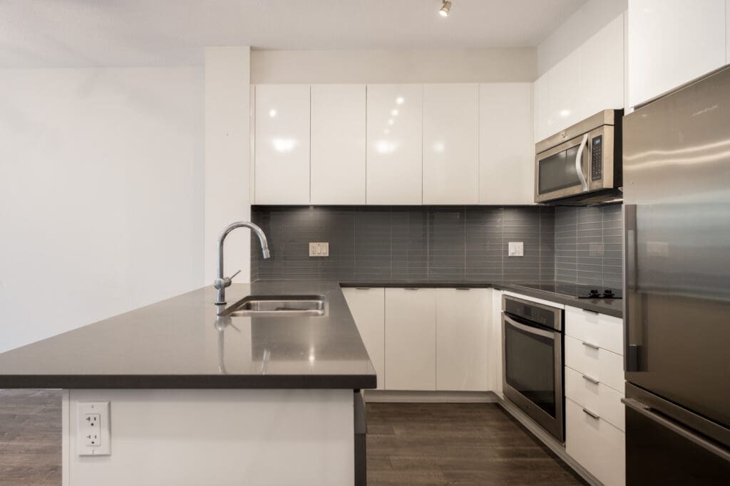 Minimalist kitchen at 2665 Mountain Hwy, North Vancouver, with white cabinets, stainless appliances, dark wood floors, and large island.