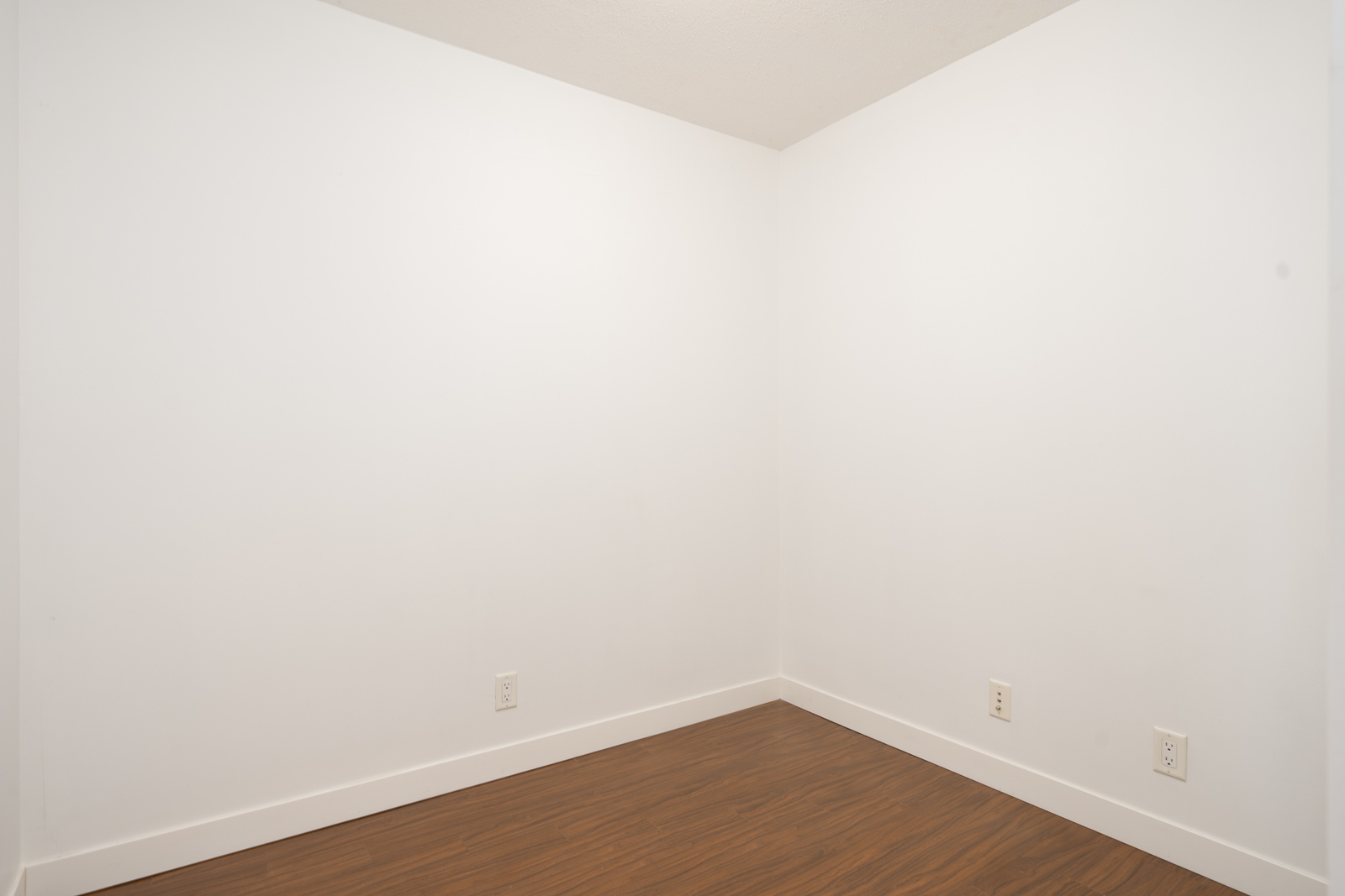 Empty room with white walls, white baseboards, and brown wood floor on 6th floor, 8033 Saba Road, Richmond. Three outlets visible.