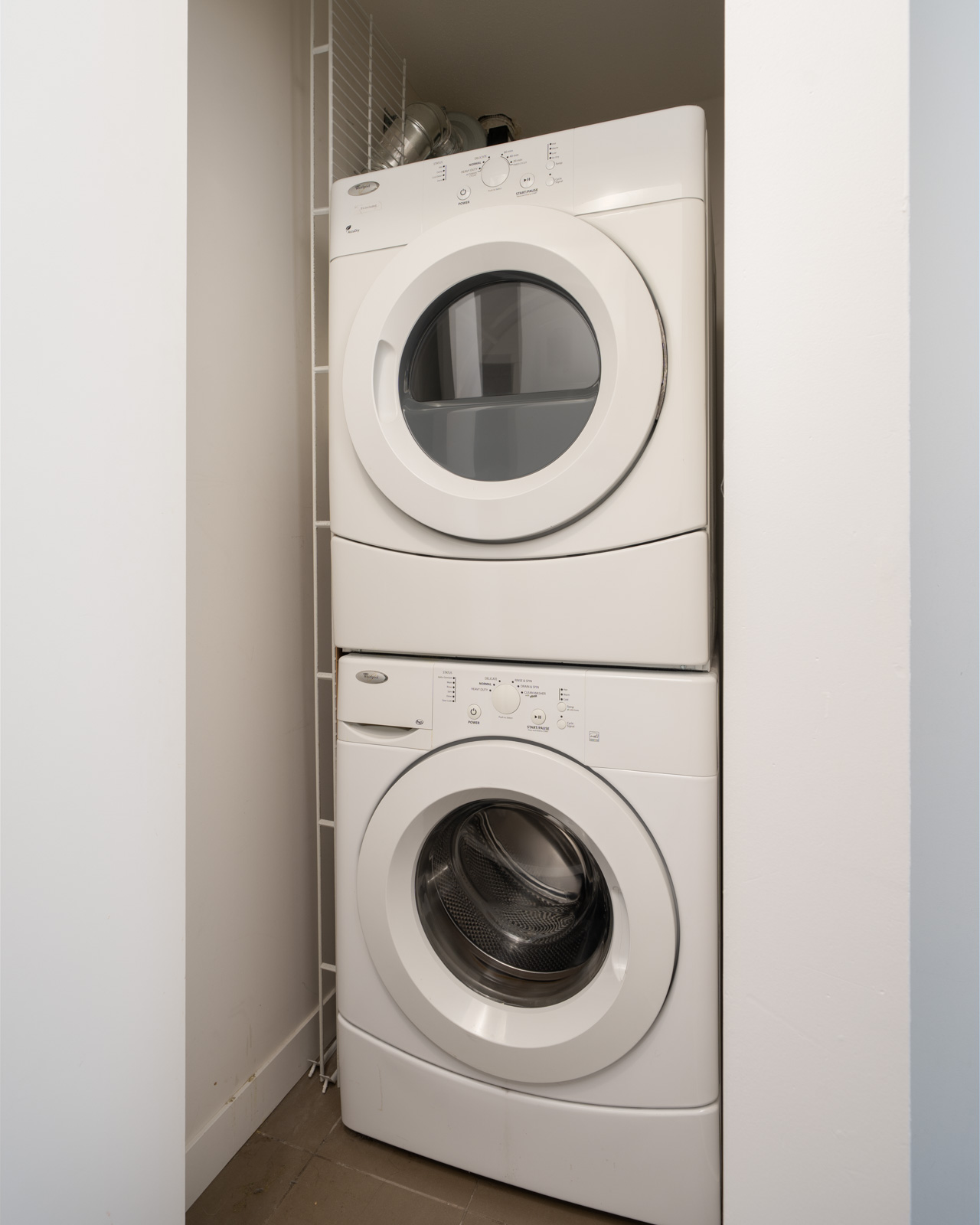 White front-loading washer and dryer stacked in a compact laundry closet with light walls and tile floor in a Richmond home at 8033 Saba Road.