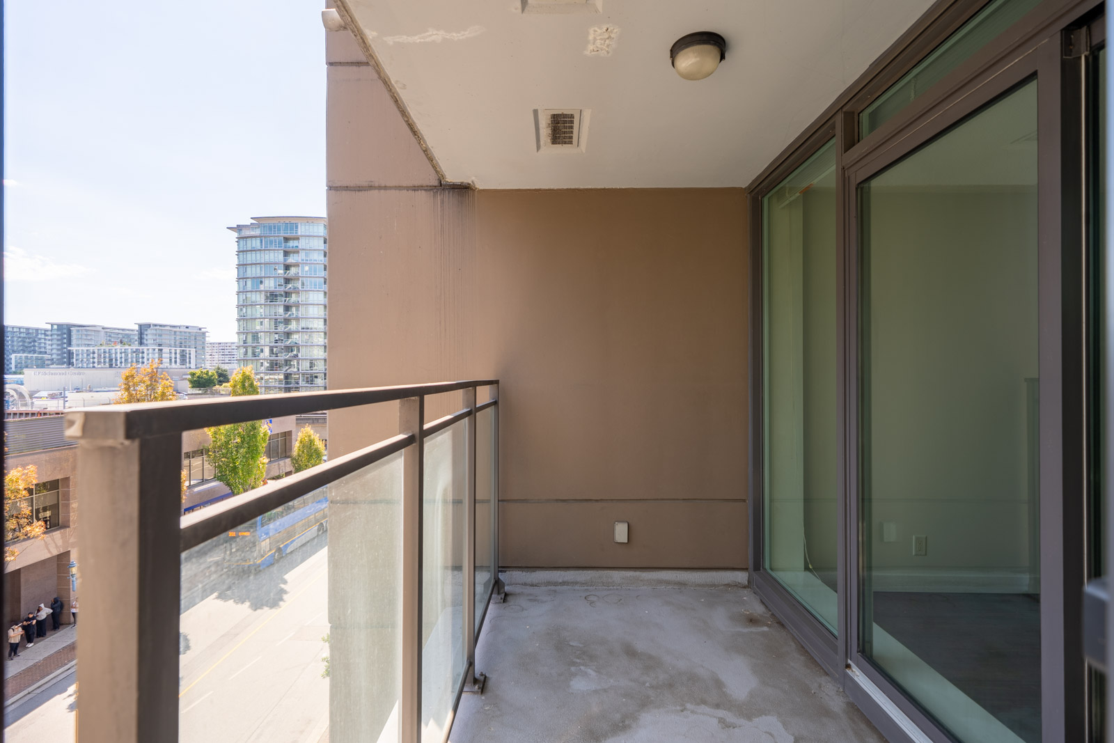 Sixth-floor balcony with glass railing, beige wall, and concrete floor overlooking city street in Richmond at 8033 Saba Road.