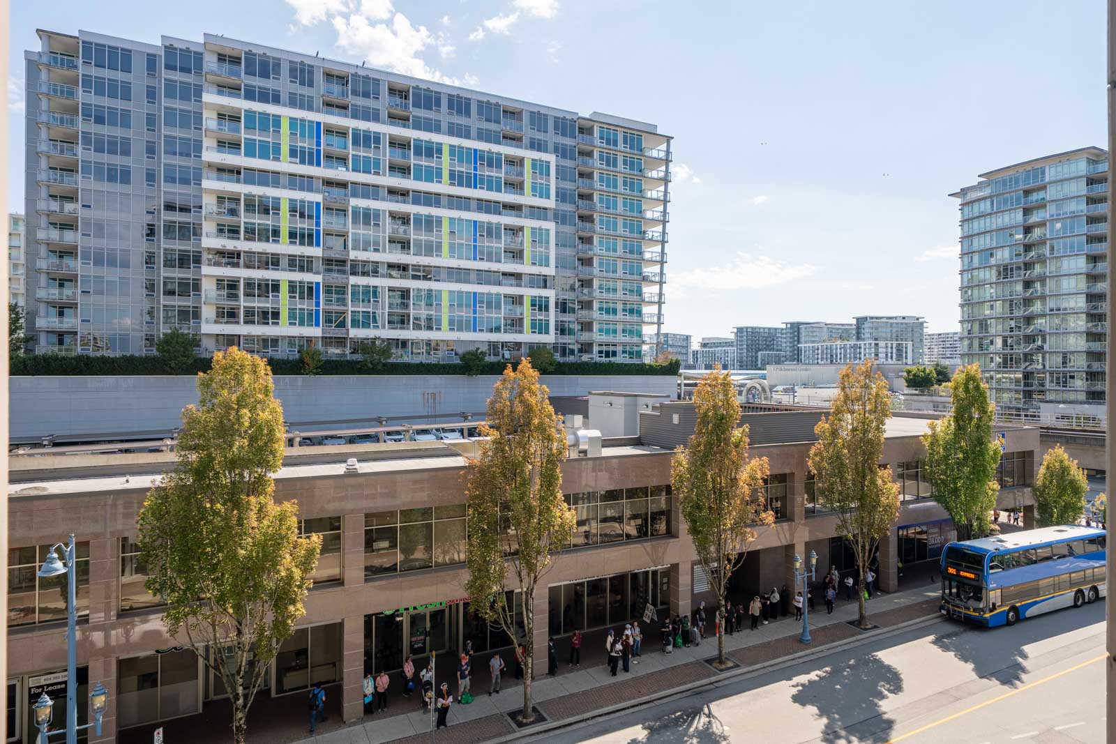 People line up outside a modern building at 8033 Saba Road, Richmond; a bus and tall apartments are visible on a sunny day.