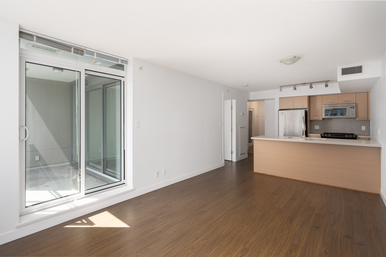Unfurnished apartment in Richmond with wood floors, open kitchen with stainless appliances, and balcony via sliding glass doors.
