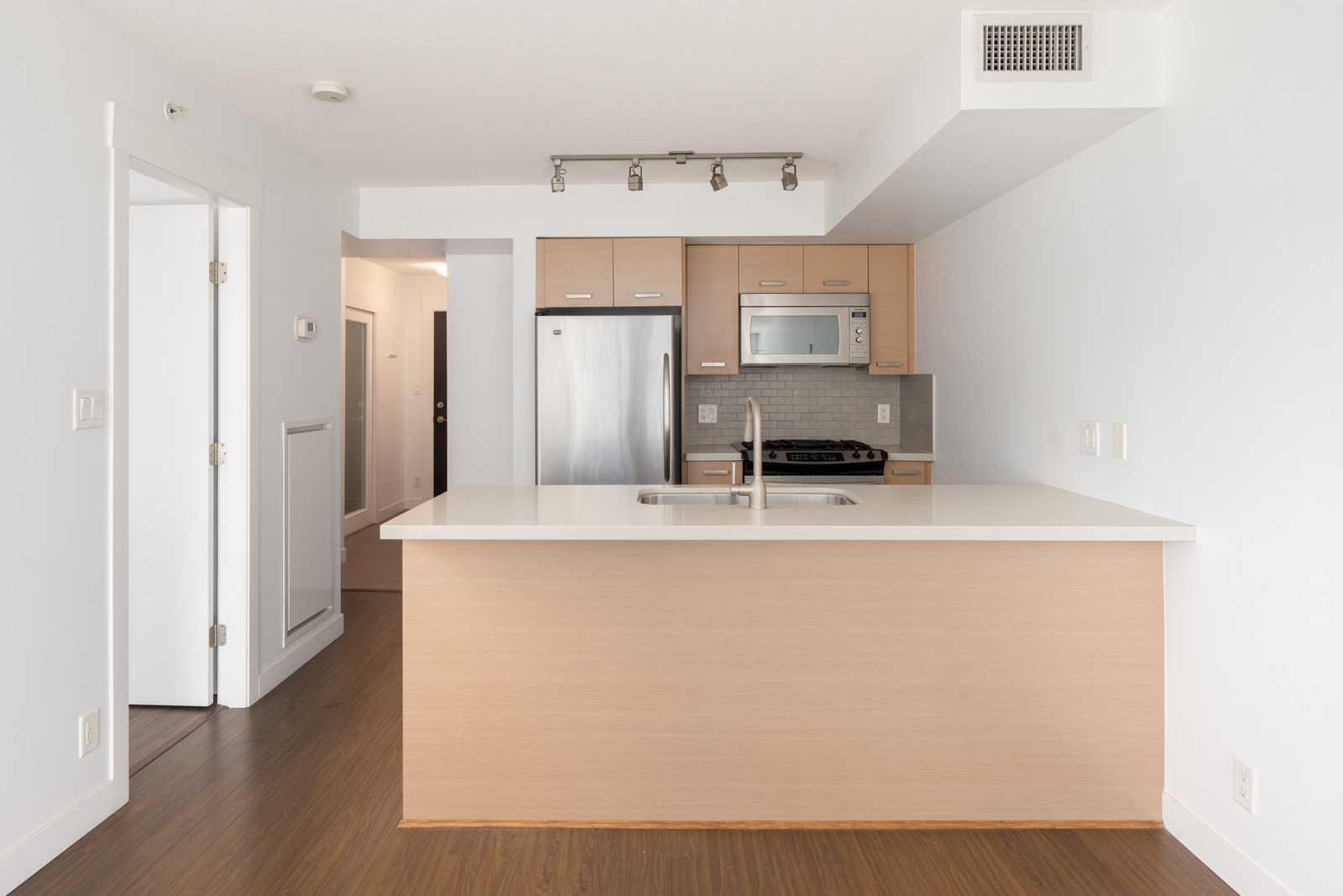 Modern kitchen with light wood cabinets, stainless steel appliances, island sink, white counters, dark wood floors in Richmond at 8033 Saba Road.