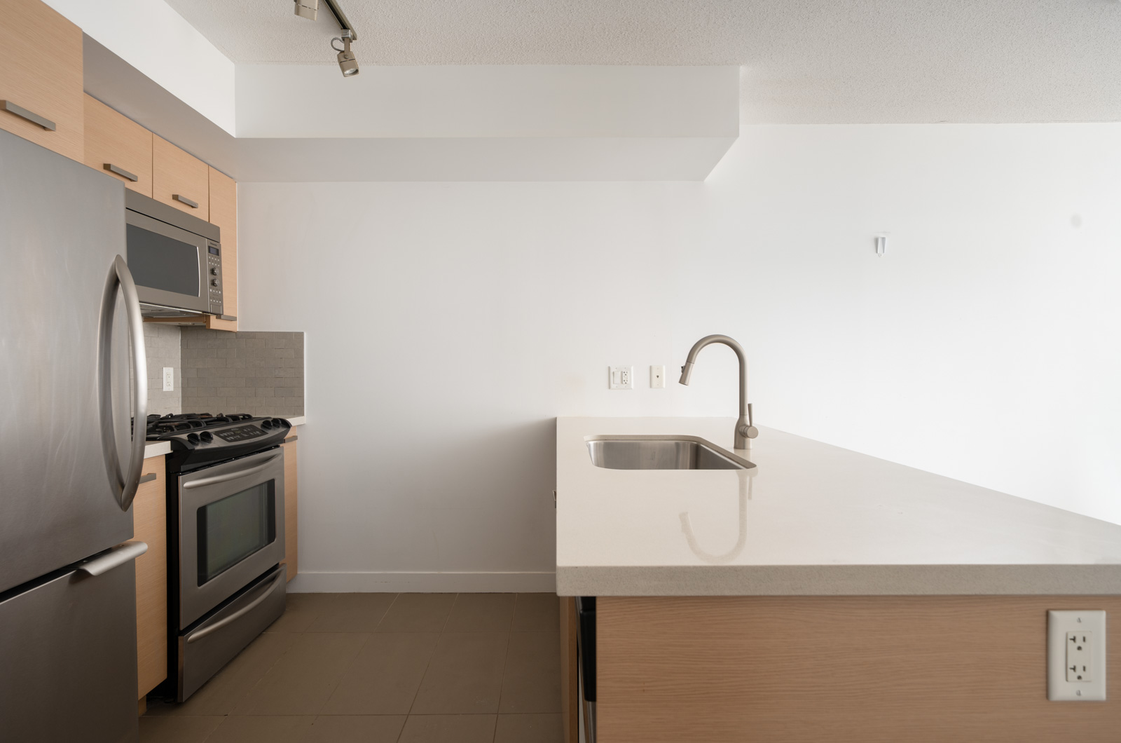 Modern kitchen with stainless steel appliances, light wood cabinets, built-in microwave, and large island with sink in Richmond.