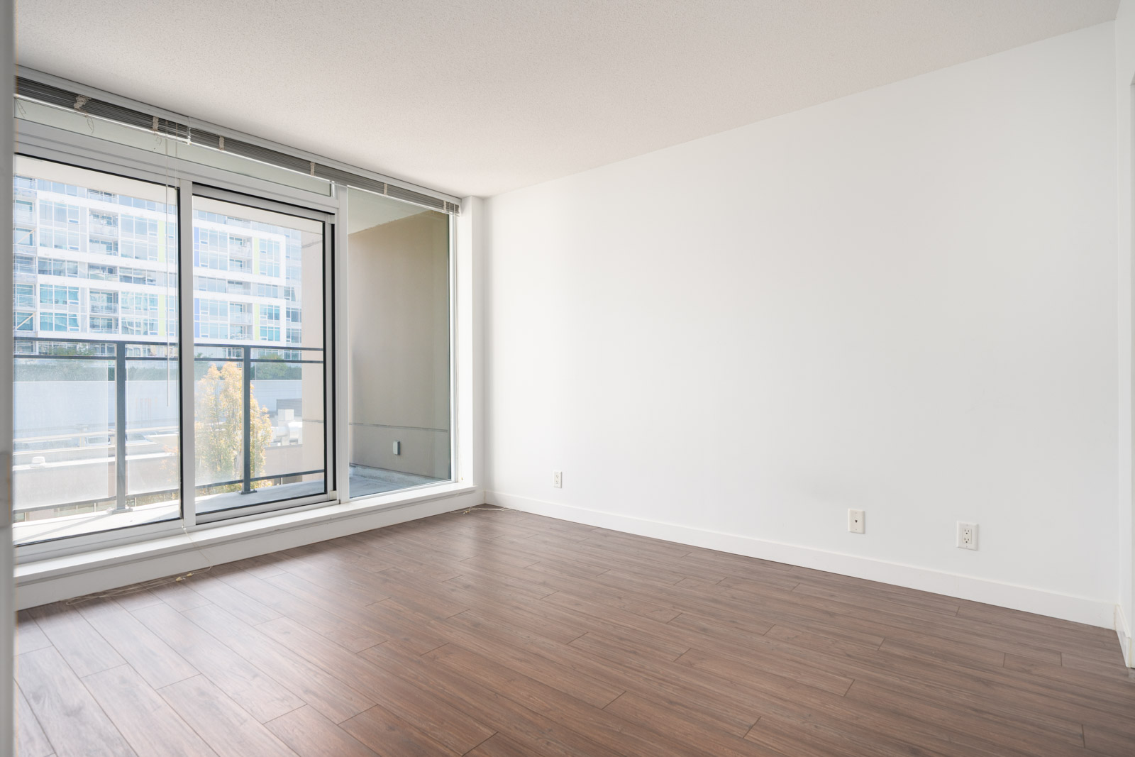 Empty room with white walls, wood floors, floor-to-ceiling windows, and partial balcony view on the 6th floor in Richmond.