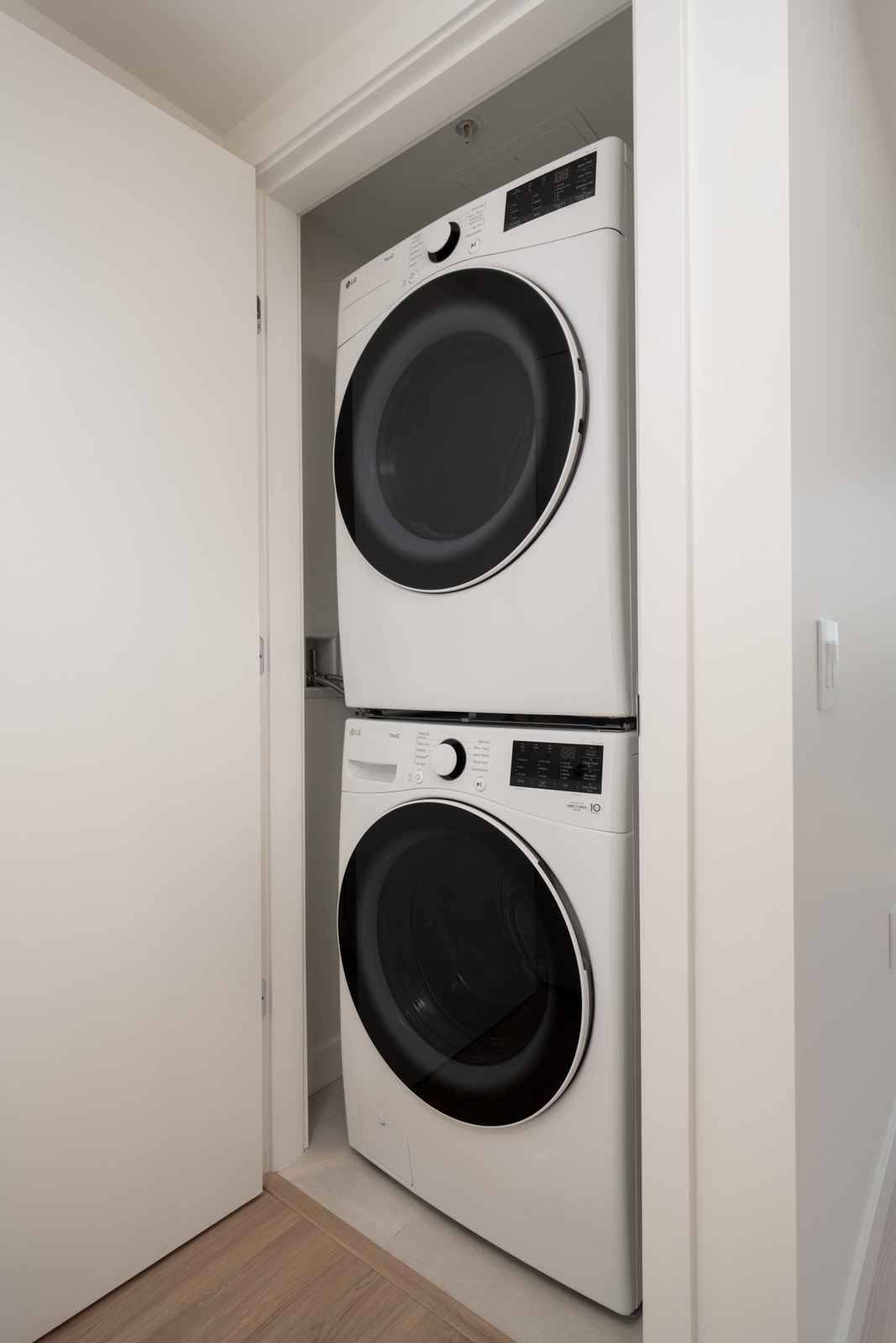 A stacked washer and dryer set is installed in a small laundry closet with white walls and a partially open door.