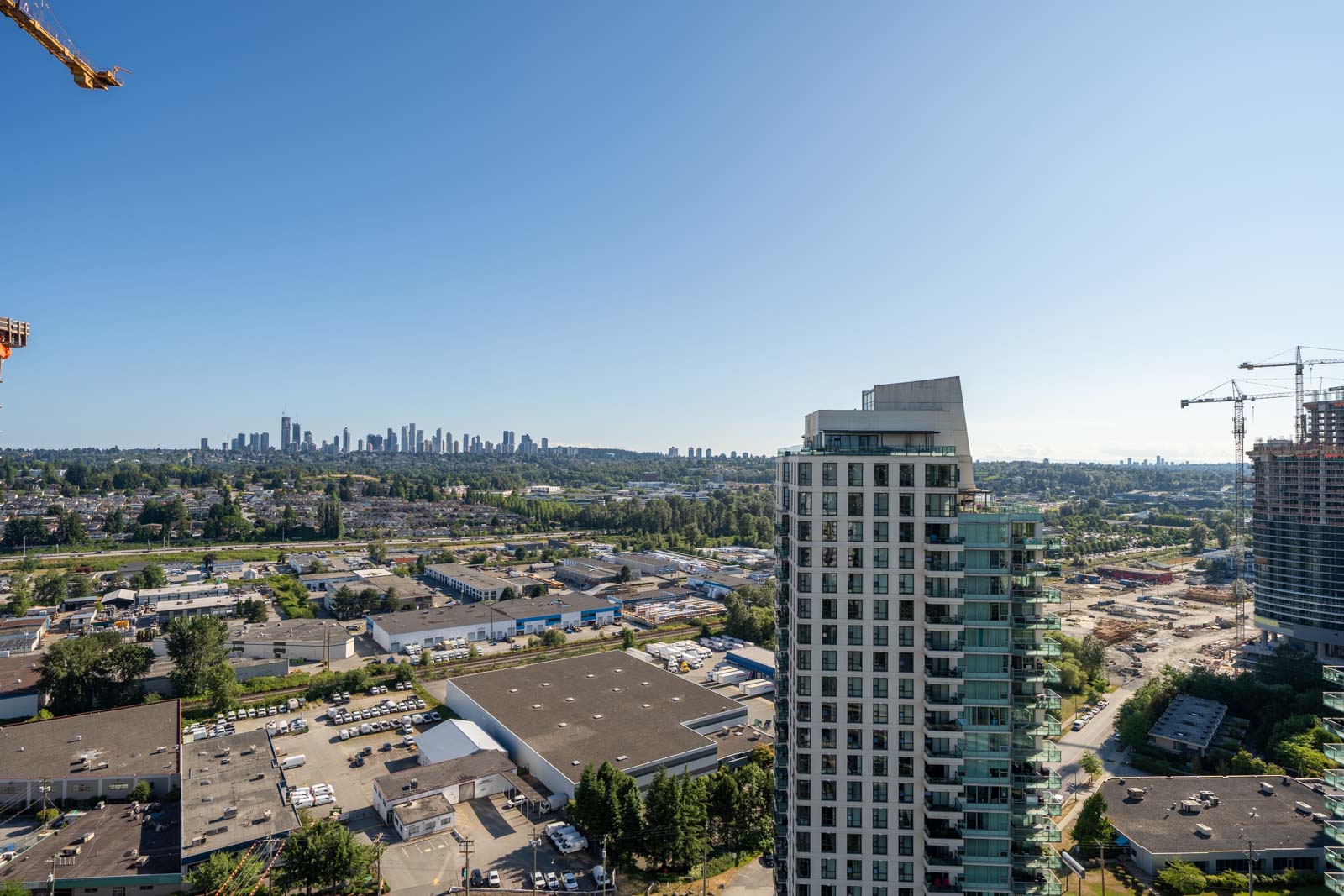 A high-rise building stands in the foreground with a construction site and urban landscape extending into the distance under a clear blue sky.