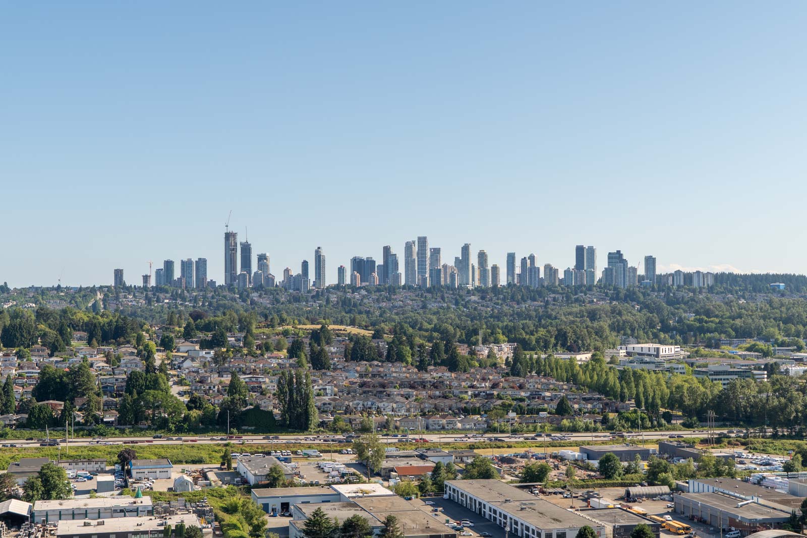 A wide-angle view of a city skyline with numerous high-rise buildings, residential neighborhoods, and industrial areas under a clear blue sky.