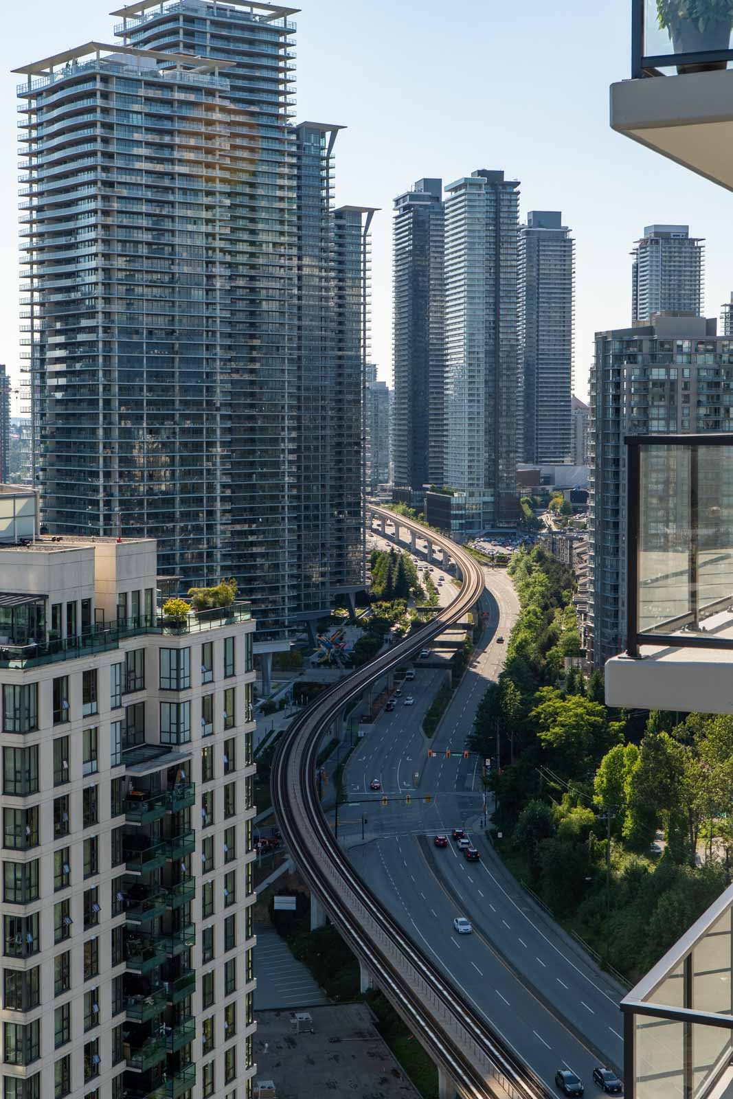 High-rise buildings surround a curved elevated train track and a multi-lane roadway on a clear day in an urban city setting.
