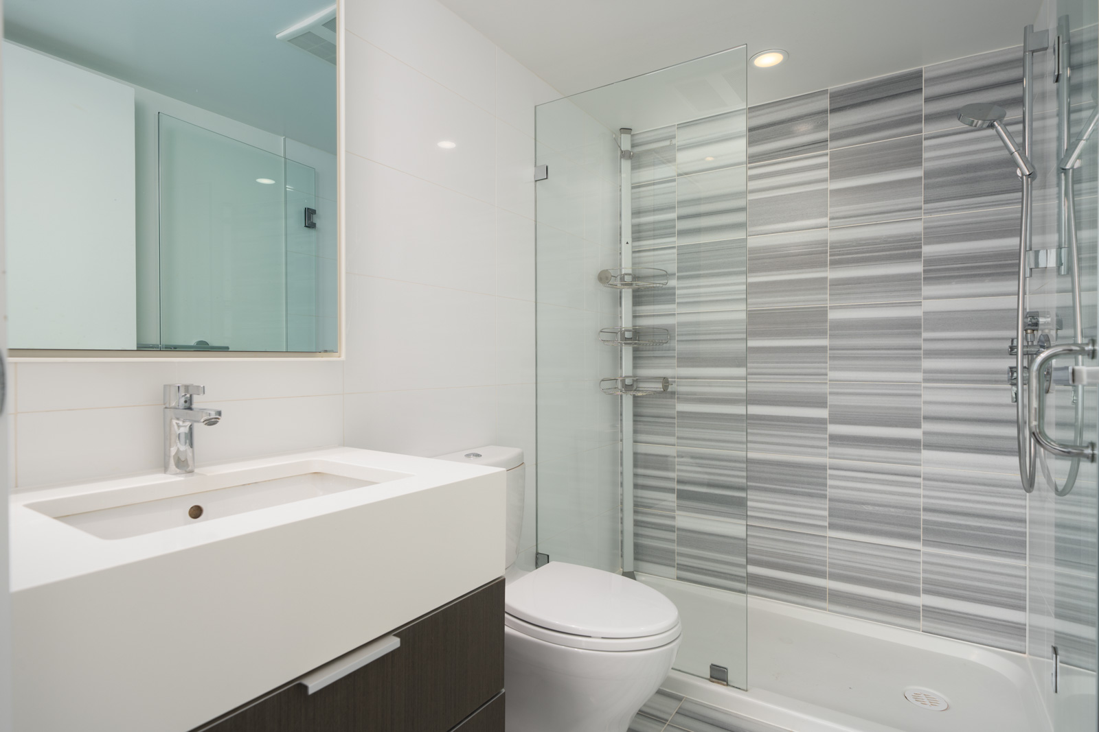 Modern bathroom with a white sink, wall-mounted faucet, toilet, and a glass-enclosed shower with gray and white striped tiles.