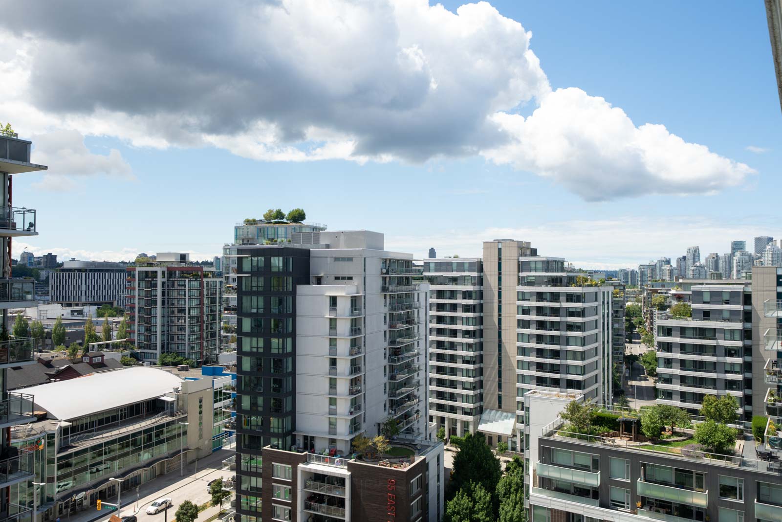 High-rise residential buildings with balconies and rooftop gardens under a partly cloudy sky in an urban cityscape.