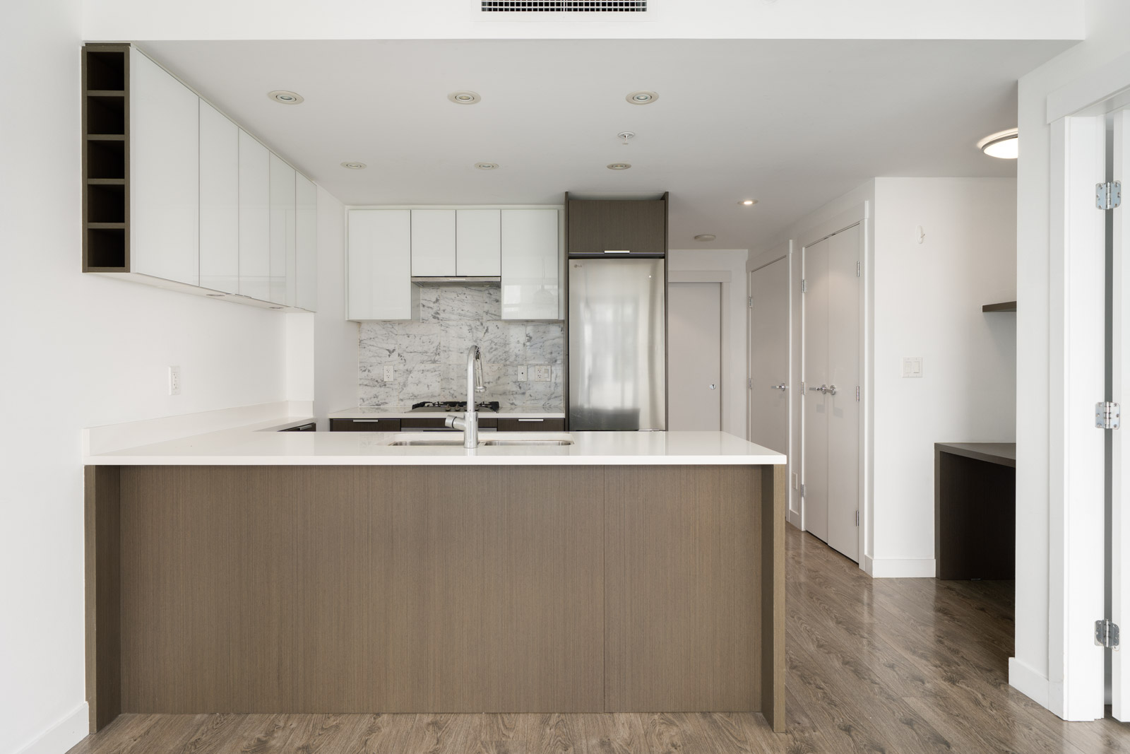 Modern kitchen with white cabinets, marble backsplash, stainless steel appliances, and a large brown island with white countertop on wood flooring.