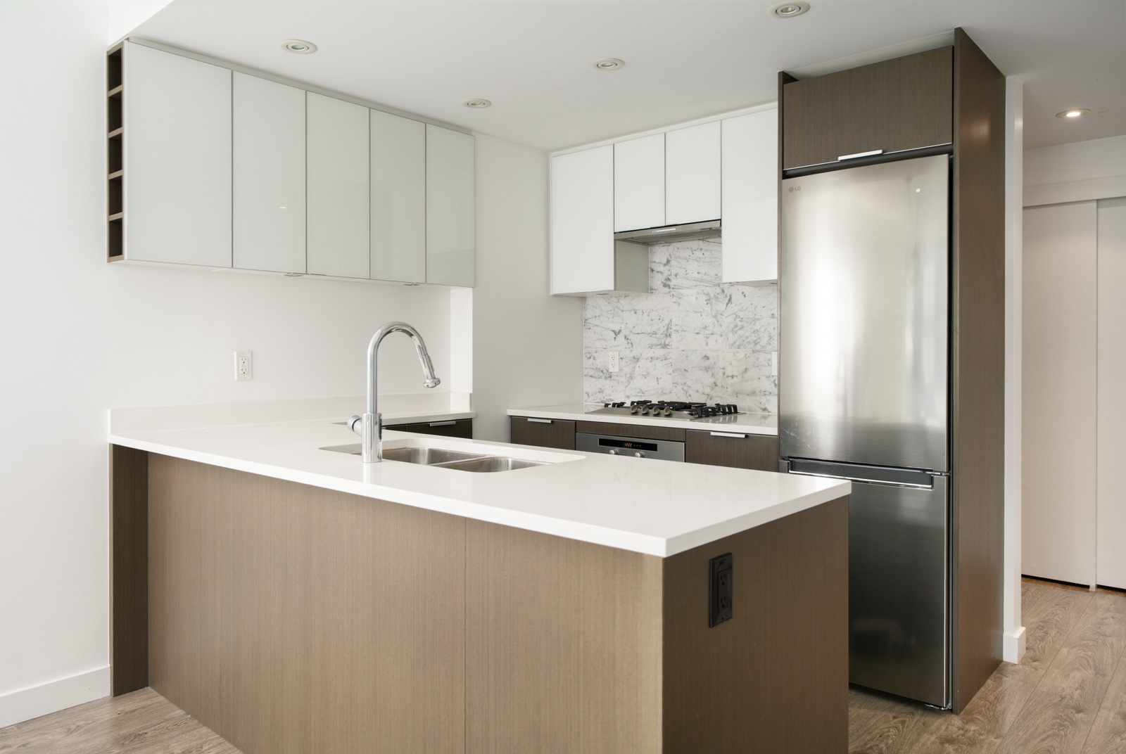 Modern kitchen with white countertops, wood cabinets, stainless steel appliances, a built-in stove, and a double sink on a central island.