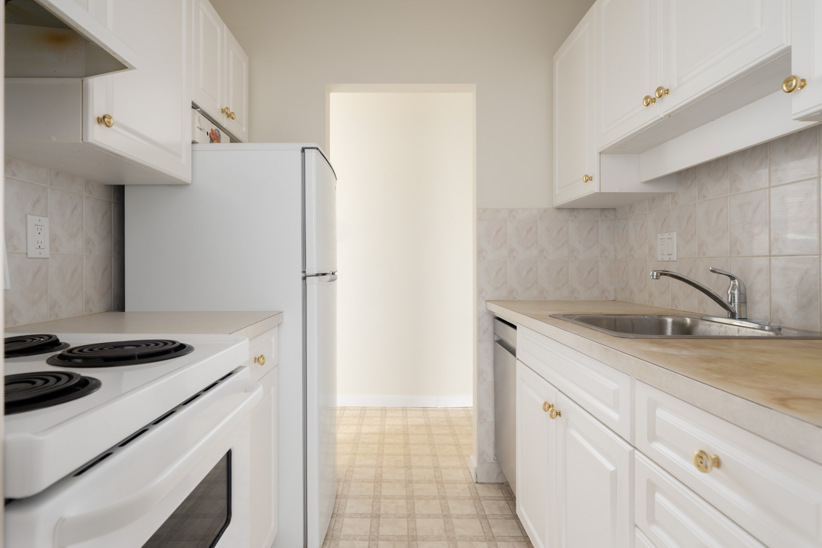 Small kitchen on W 2nd Ave, Vancouver, with white cabinets, electric stove, white fridge, beige counters, and a stainless sink.