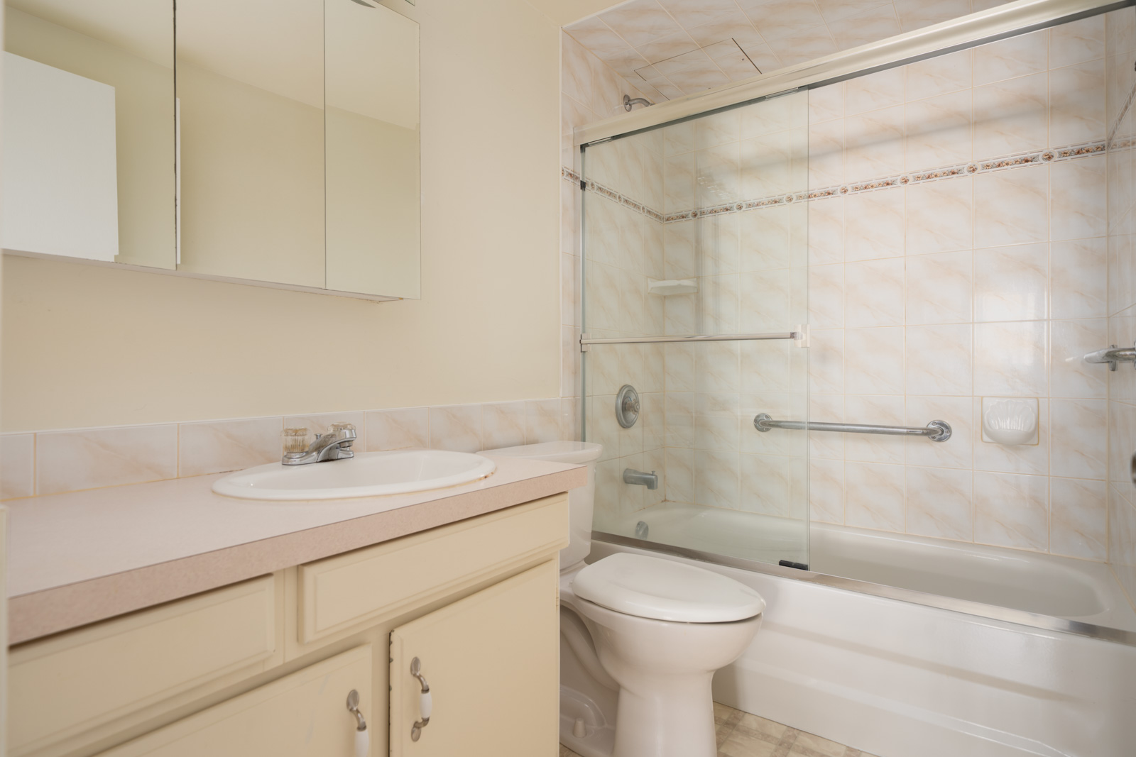 Second-floor Vancouver bathroom featuring a sink, countertop, toilet, and bathtub with sliding glass doors and beige tiled shower.