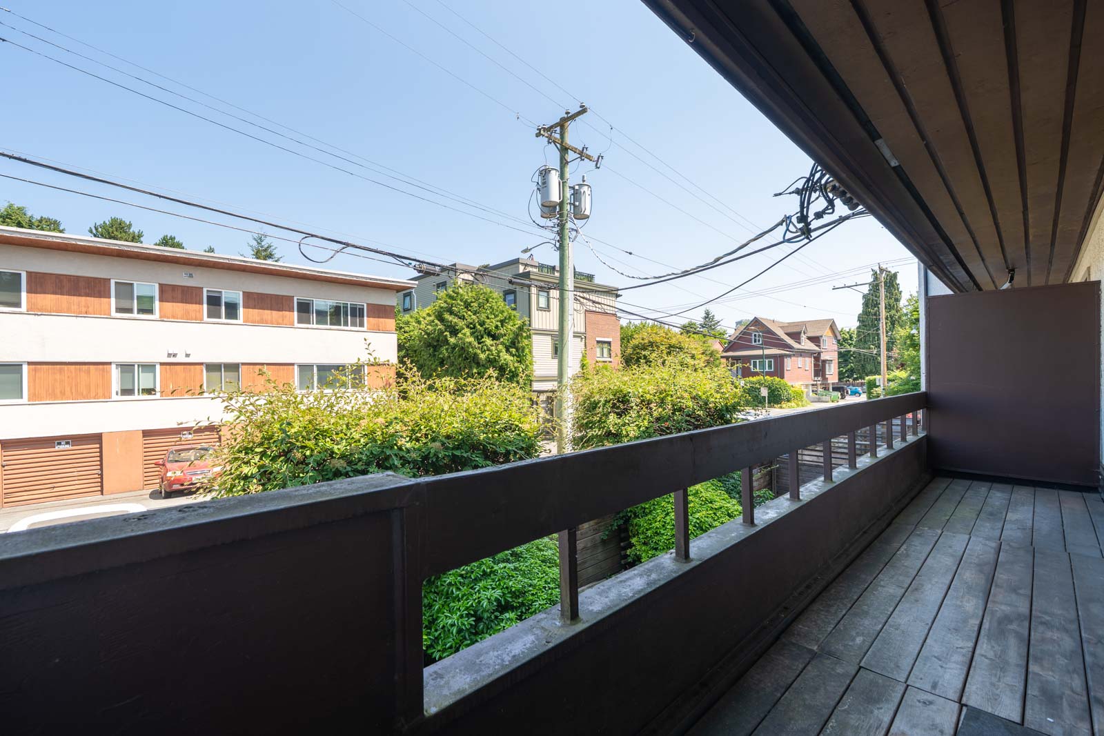 View from a second-story balcony over 2nd Avenue, Vancouver, showing homes, power lines, and greenery under a clear sky in 2025.