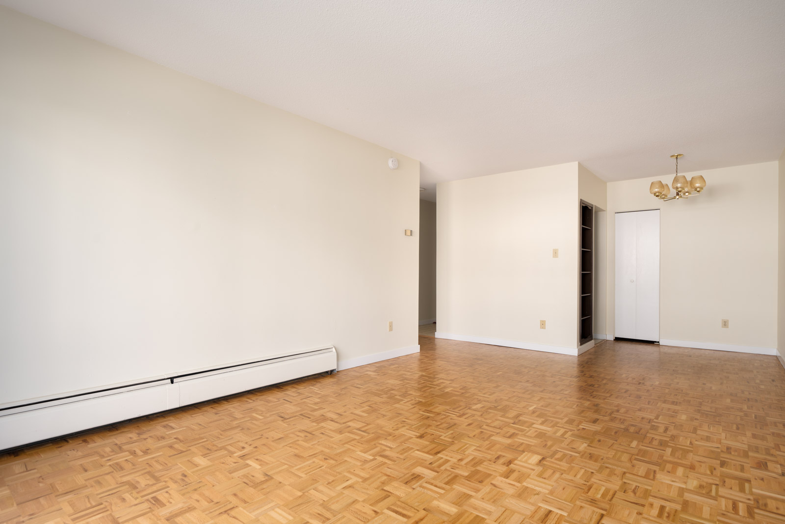 Empty room with light walls, parquet flooring, chandelier, closet door, and wall heater on 2nd floor of W 2nd Ave home in Vancouver.