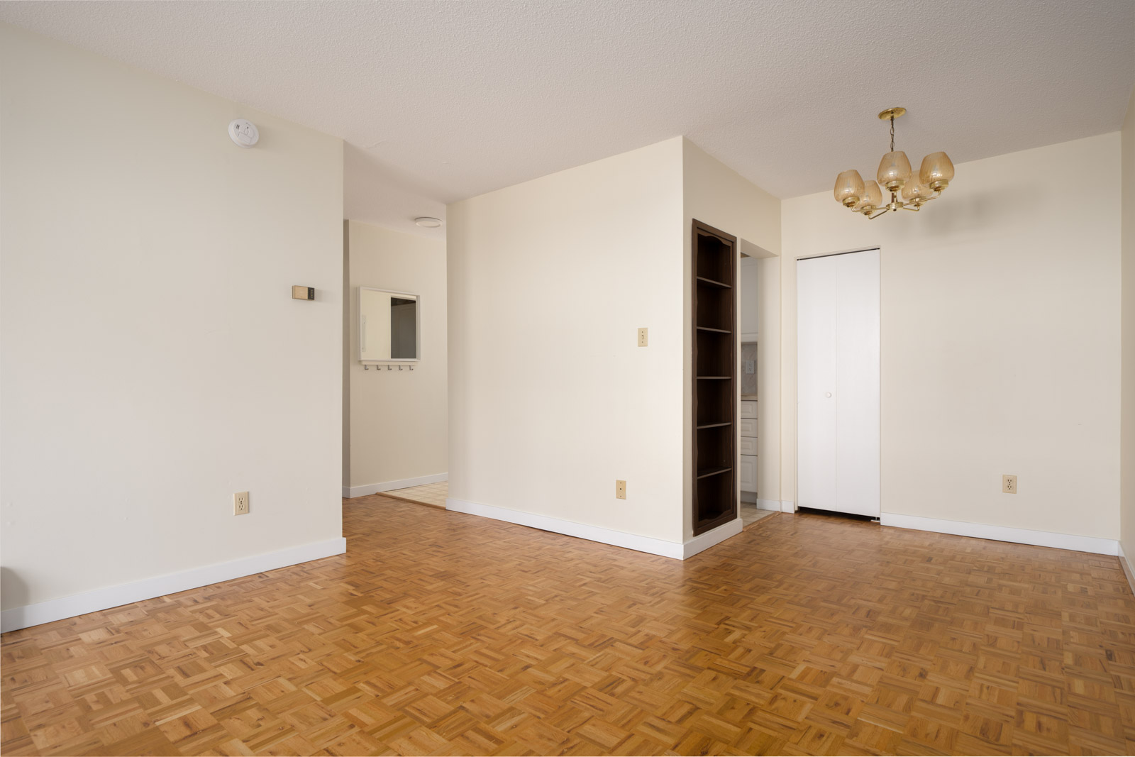 Empty room on W 2nd Ave, Vancouver with parquet floors, beige walls, built-in shelf, white closets, and brass chandelier.