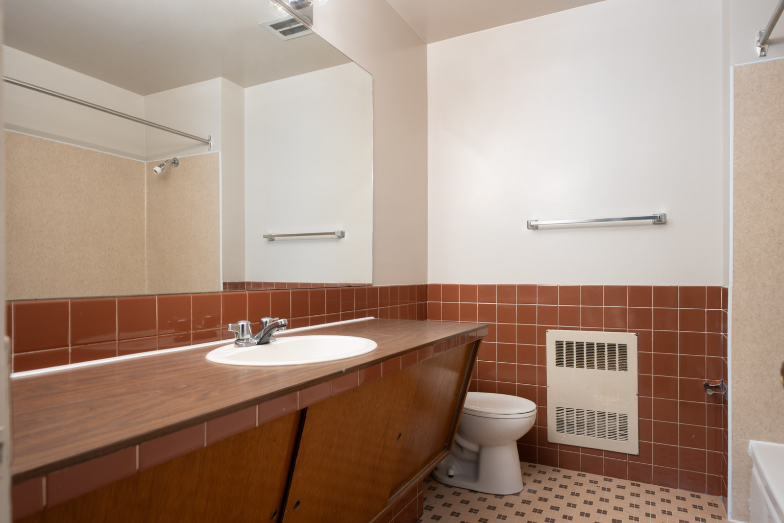 Bathroom with a large mirror, brown countertop and sink, brown tile accents, a toilet, and a bathtub with beige walls and checkered tile flooring.
