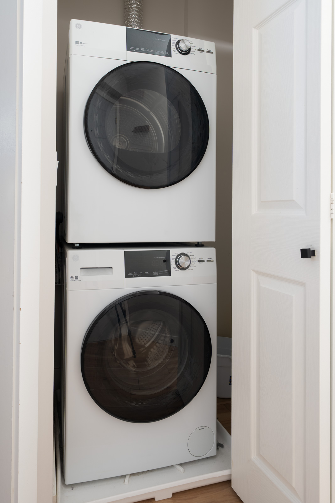 A stacked washer and dryer set is installed in a small laundry closet with a white door partially open.