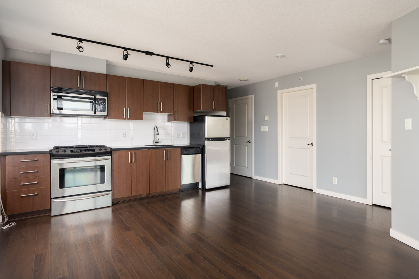 Bright, empty modern kitchen at 1068 W Broadway, Vancouver with dark wood cabinets, stainless appliances, white tile backsplash.
