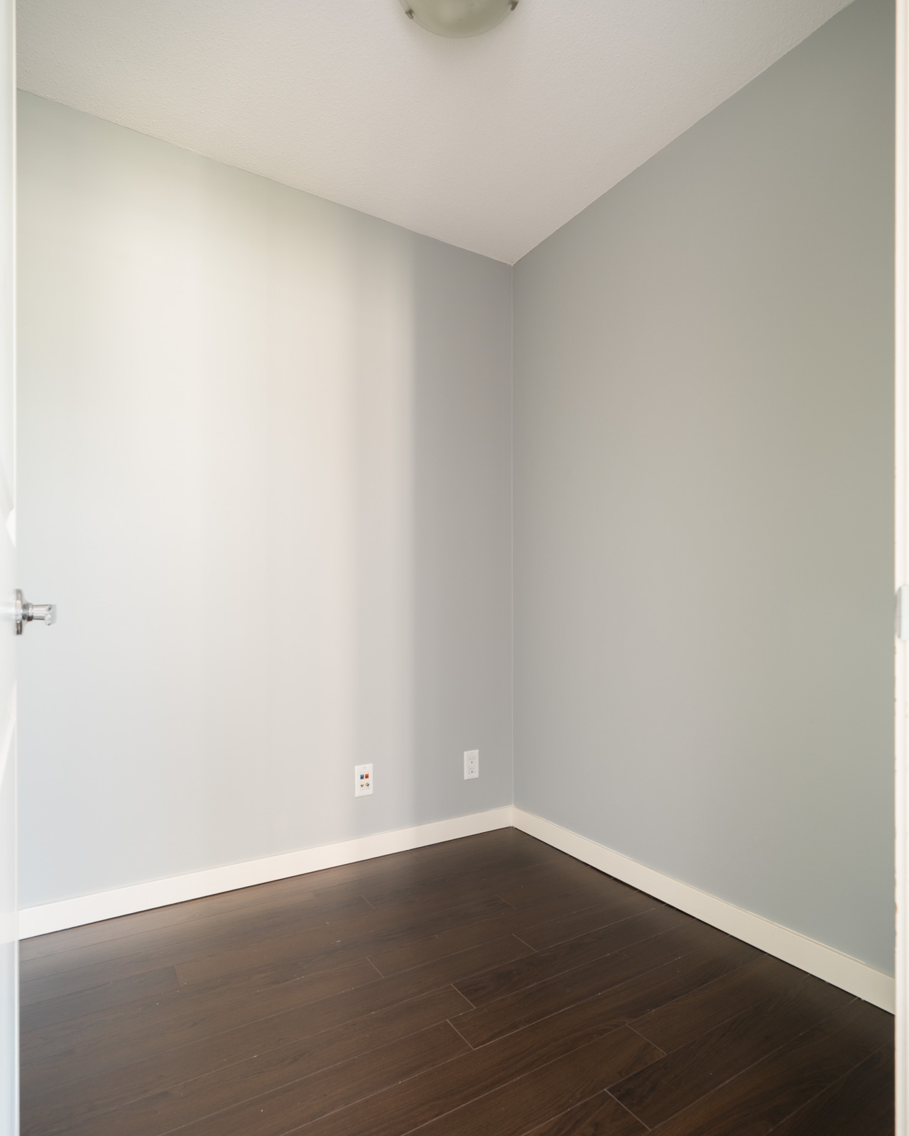 Empty room with light gray walls, dark wood flooring, ceiling light fixture, and floor-level outlets in Vancouver at 1068 W Broadway.