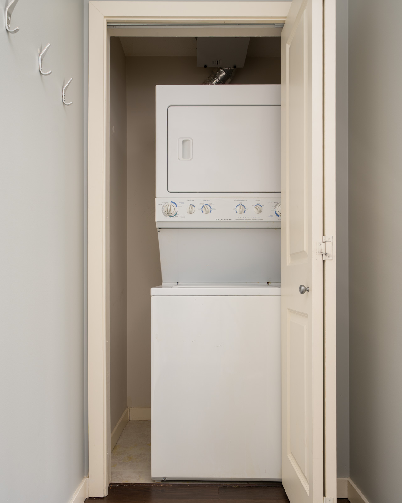 Stacked washer and dryer in a small open closet with neutral walls and hooks on the left at 1068 W Broadway, Vancouver.