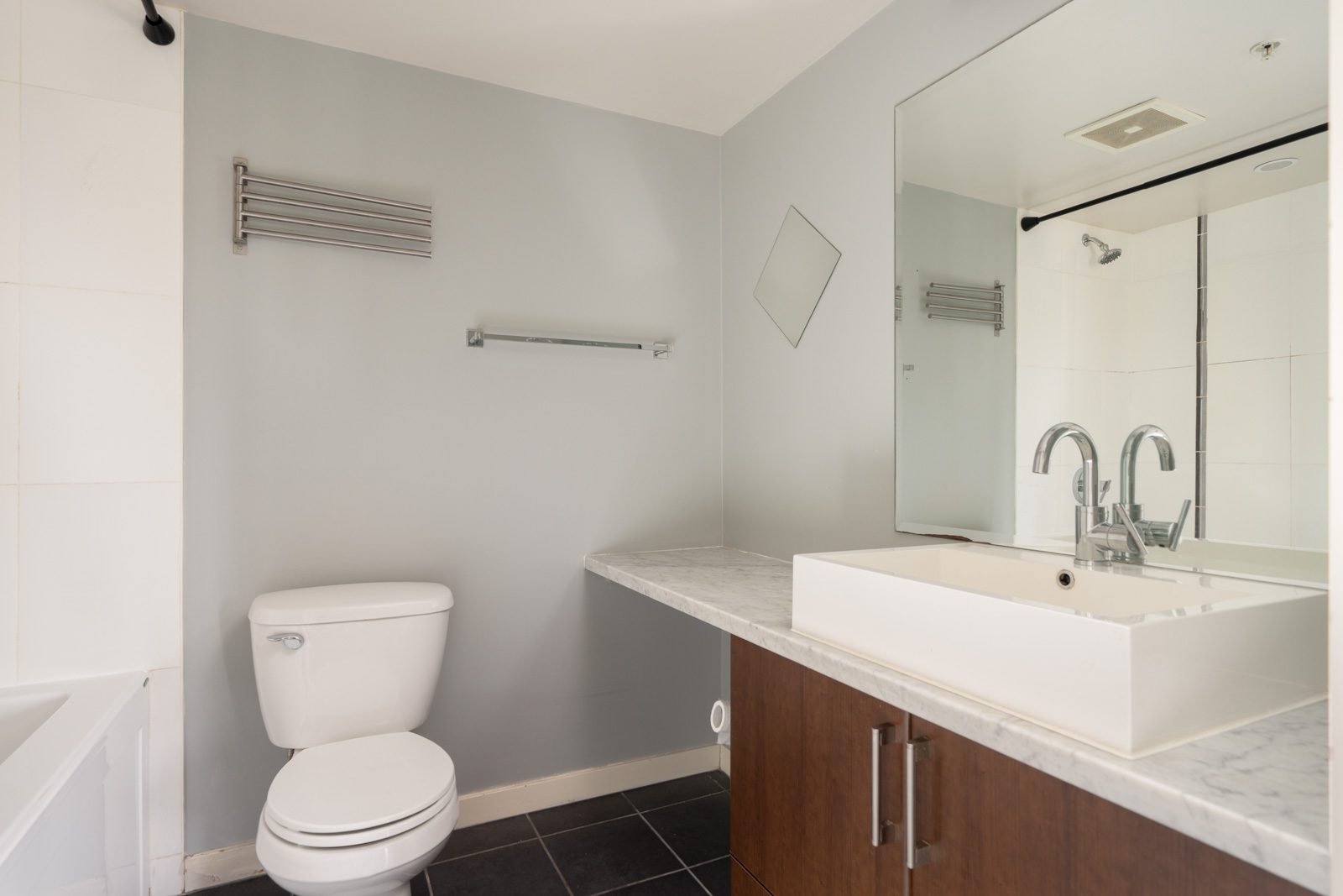 Modern Vancouver bathroom at 1068 W Broadway with toilet, marble sink, large mirror, towel bars, and gray walls.