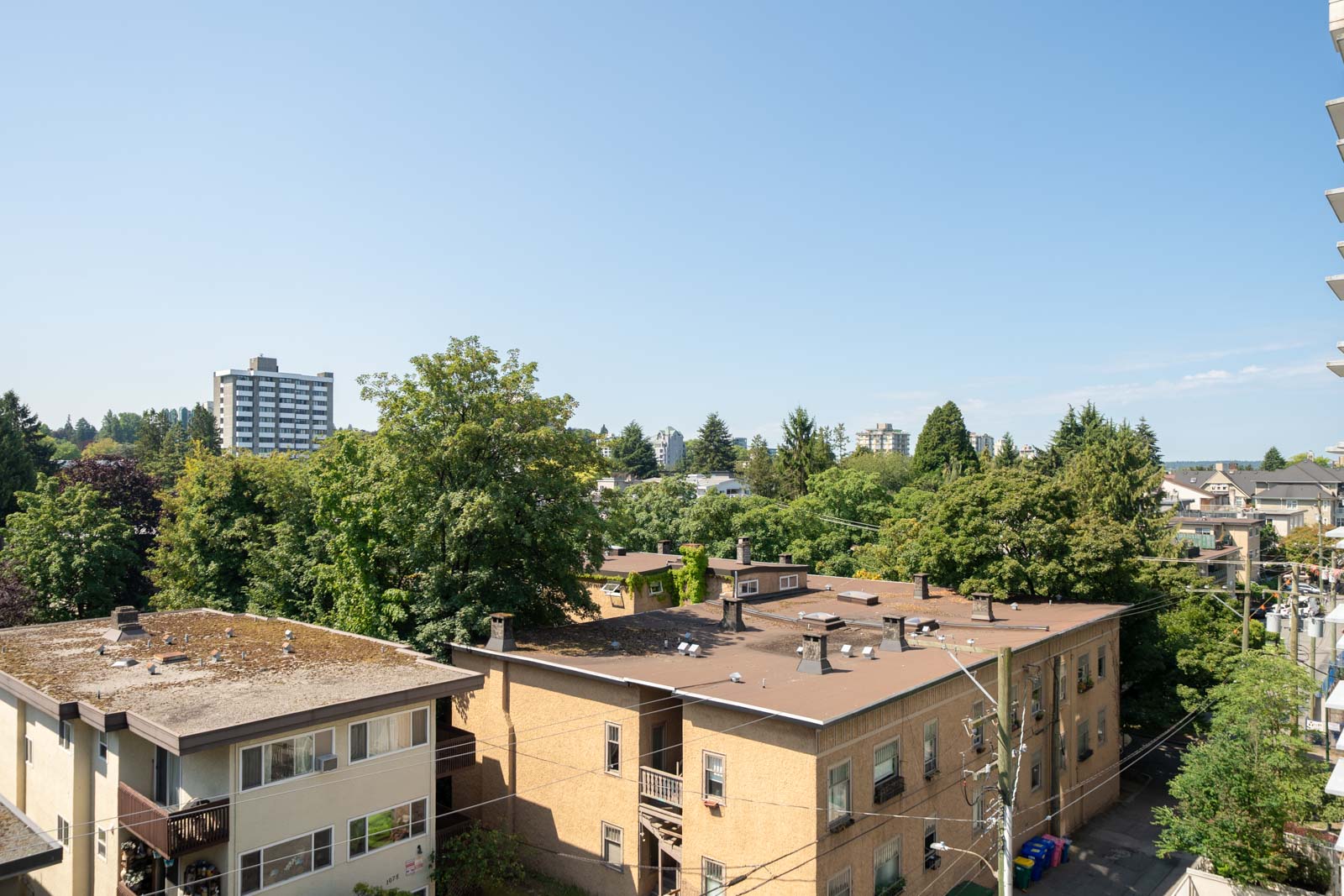 Residential buildings with flat roofs amid trees under a clear blue sky near 1068 W Broadway, Vancouver.