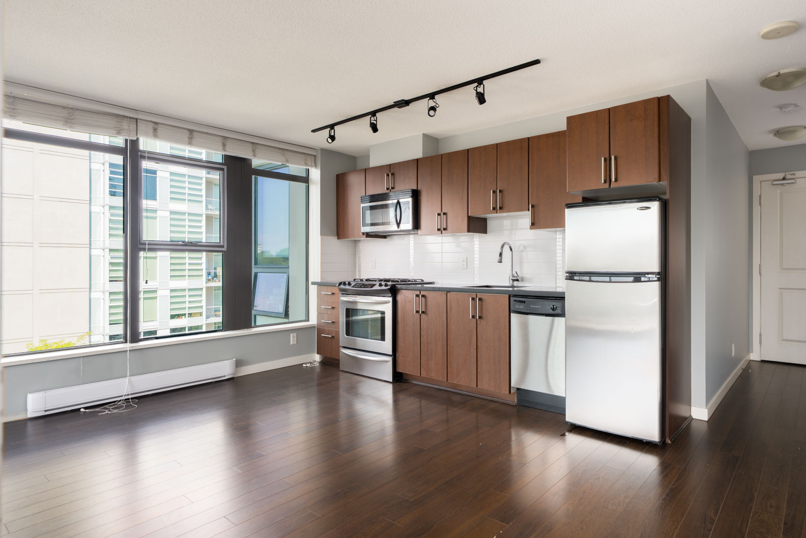 Vancouver apartment kitchen with stainless appliances, dark wood cabinets, track lighting, large windows, and hardwood floors.