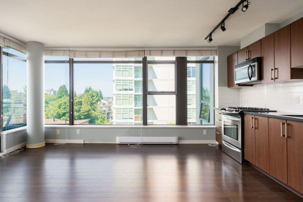 Modern apartment at 1068 W Broadway, Vancouver, with big windows, wood floors, dark kitchen cabinets, and city views.