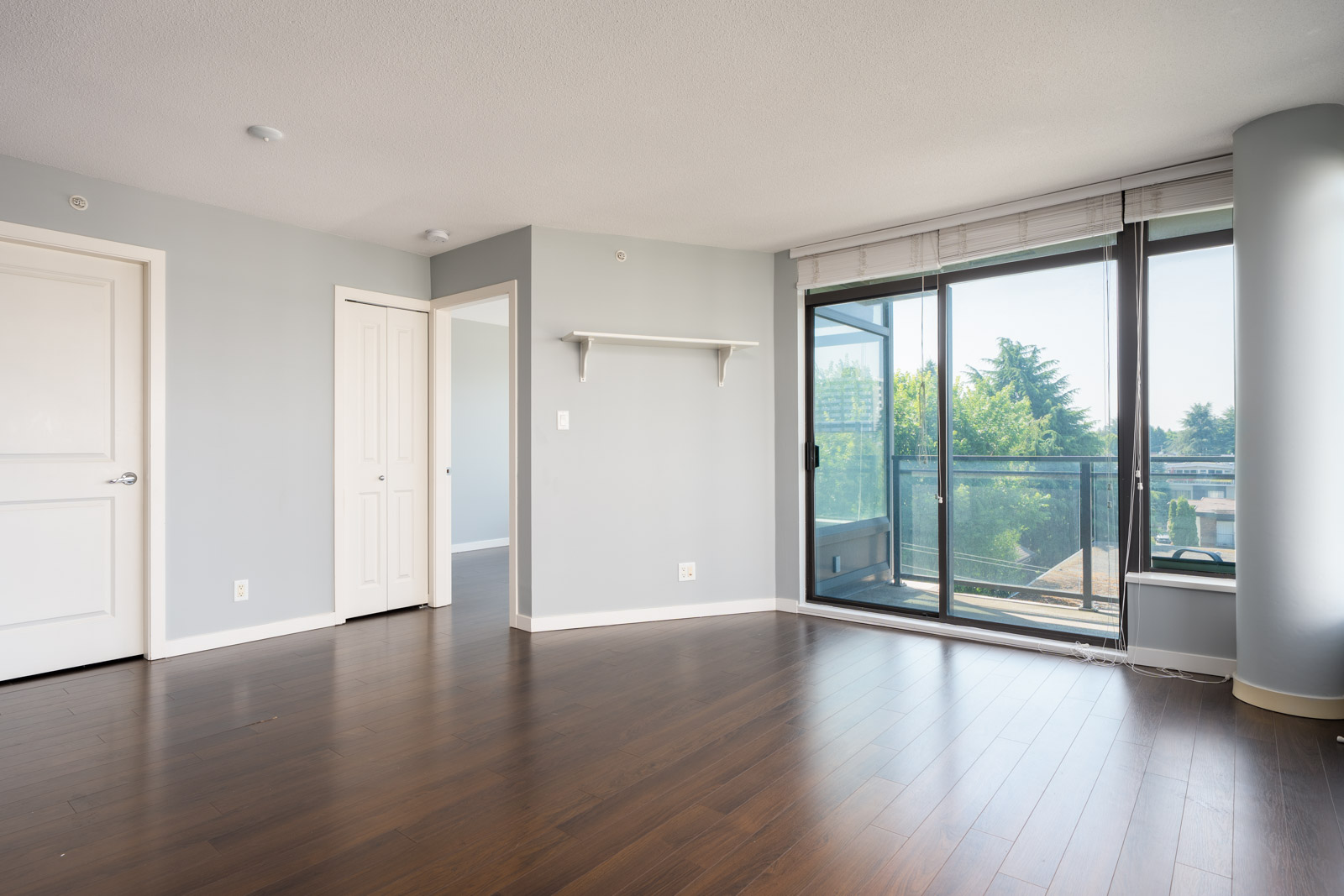 Unfurnished room at 1068 W Broadway, Vancouver with light gray walls, dark wood floor, shelf, two doors, and balcony access.